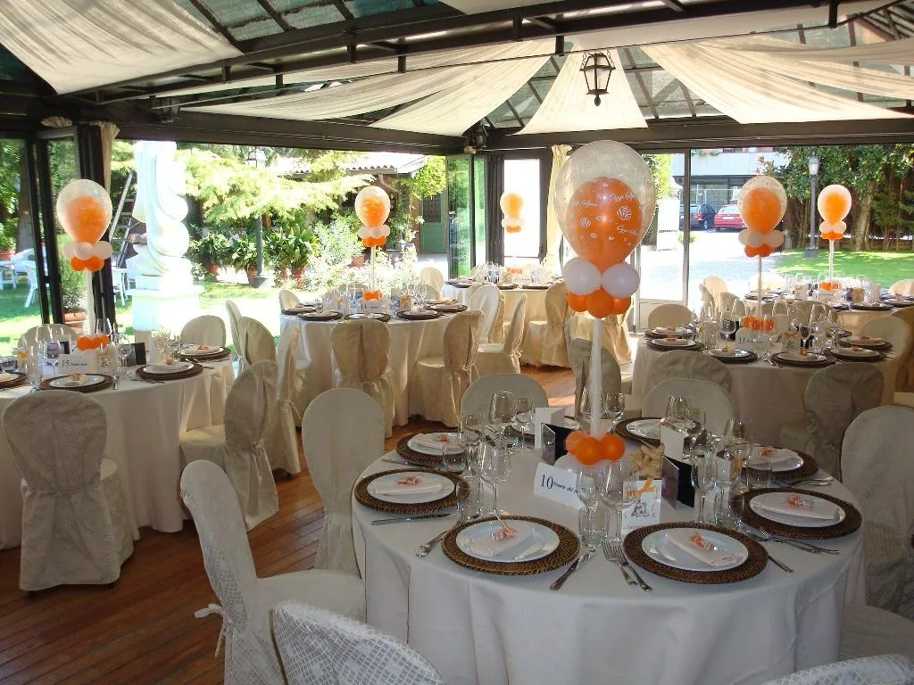 Sala del ricevimento sotto la veranda con centrotavola alti di palloncini bianchi e arancio e una bubble trasparente stampata con i nomi degli sposi