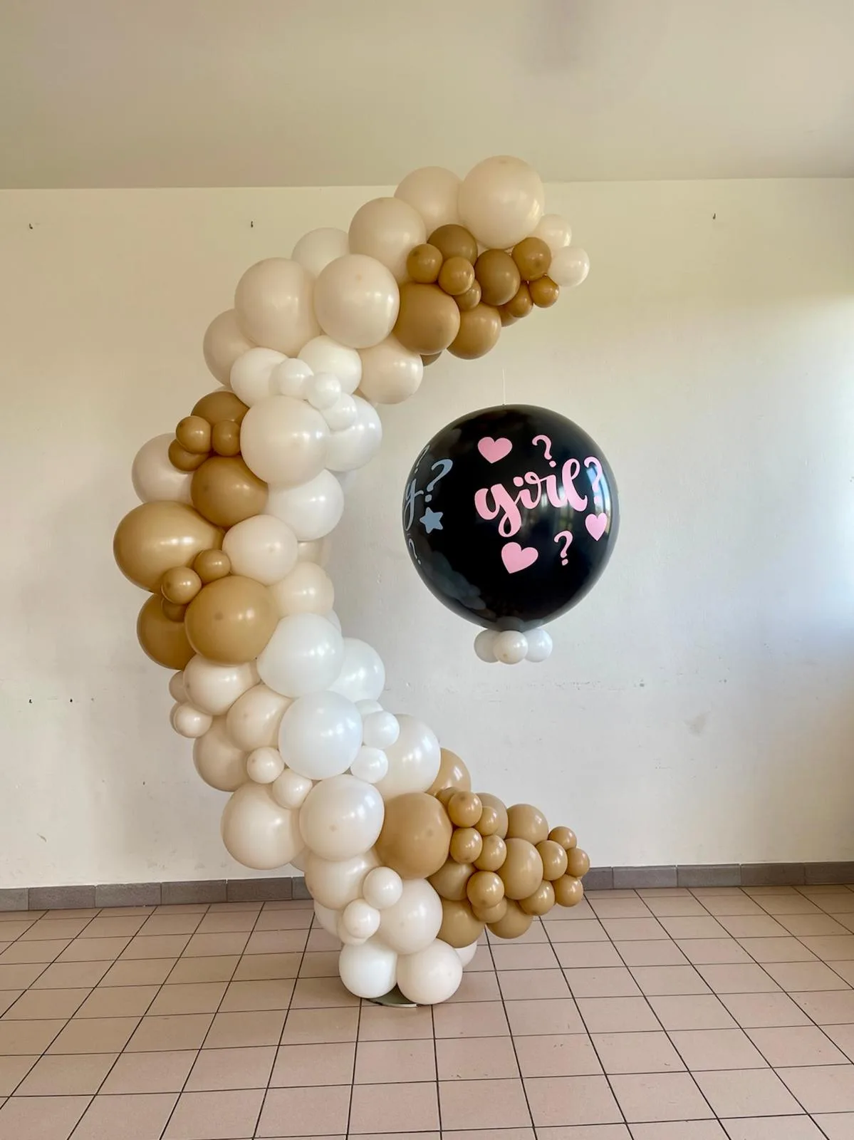 Arco di palloncini panna, bianchi e senape con il palloncino nero girl appeso al centro, allestito in una sala dalle pareti chiare