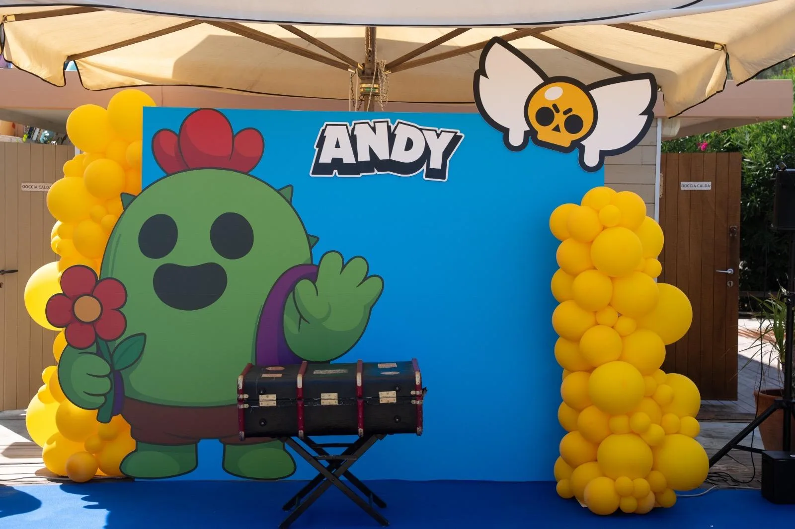 Fondale azzurro a tema Brawl Stars con il nome Andy, sagoma del personaggio cactus e due colonne di palloncini gialli, allestito sotto l'ombrellone