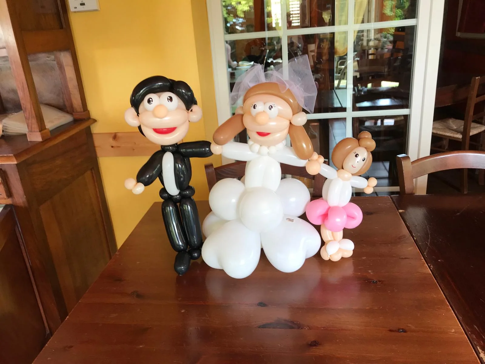 Sculture di palloncini modellabili che ritraggono lo sposo in smoking, la sposa con il velo e una bambina, appoggiate sul tavolo