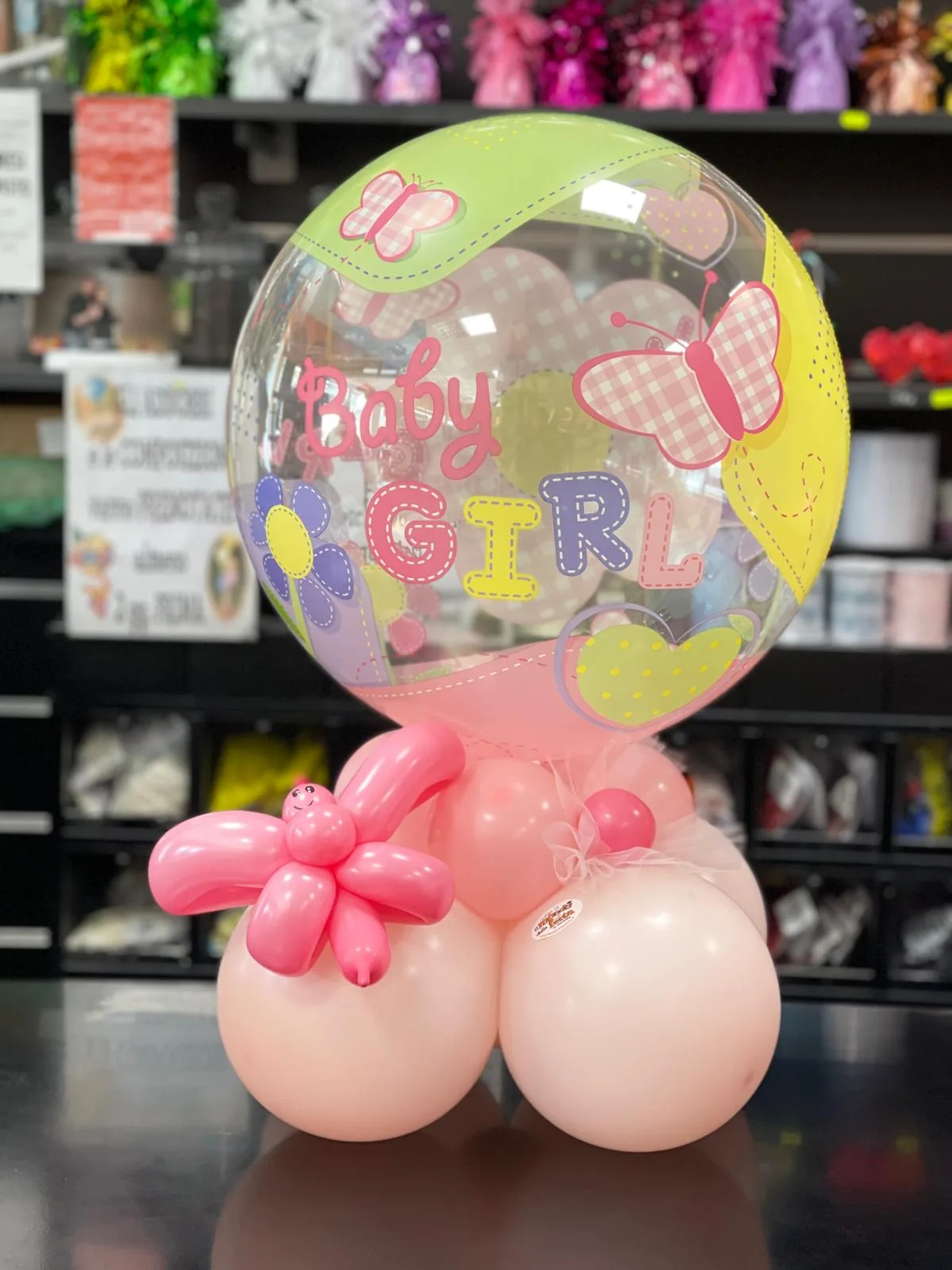 Composizione da tavolo pronta in negozio con palloncino bubble Baby Girl, base di palloncini rosa e una farfalla modellata a mano