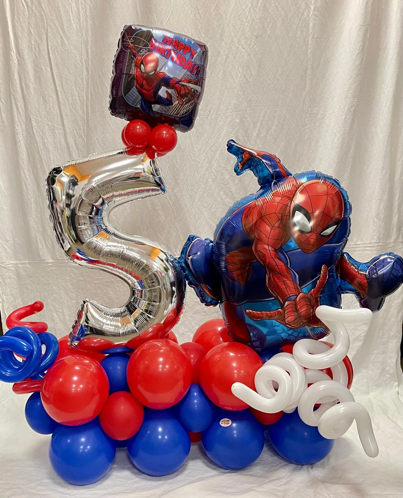 Composizione con numero 5 argento, palloncino sagomato dell'uomo ragno, base di palloncini rossi e blu e spirali bianche