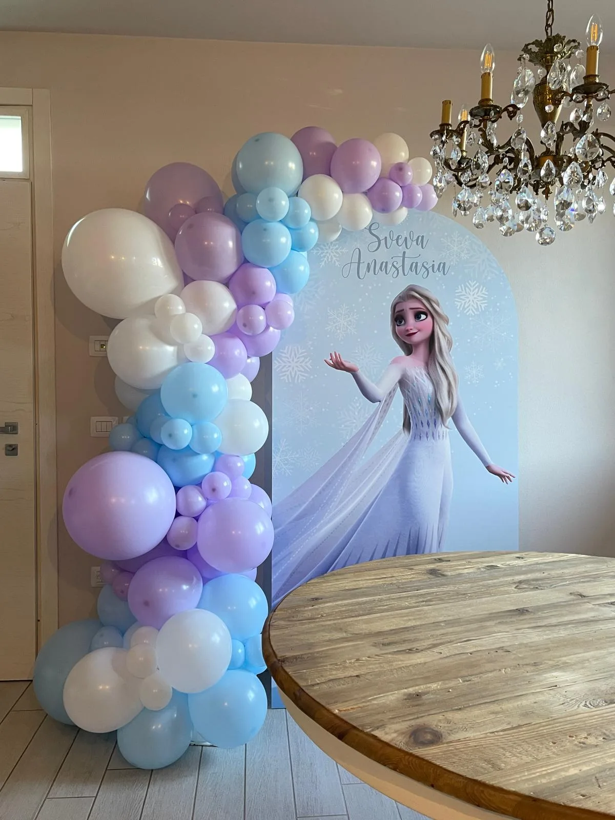 Pannello ad arco a tema Frozen con i nomi Sveva e Anastasia e ghirlanda organica di palloncini lilla, azzurri e bianchi, montato in casa