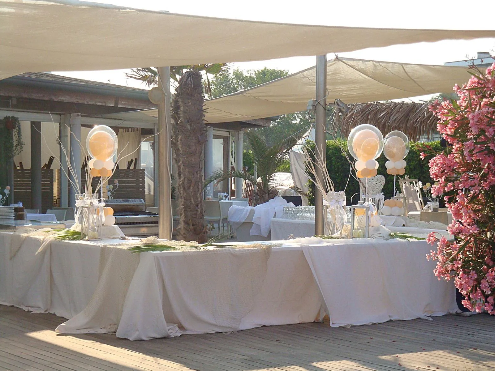 Buffet allestito in stabilimento sul mare con centrotavola di bubble trasparenti e palloncini pesca, sotto le vele di tessuto