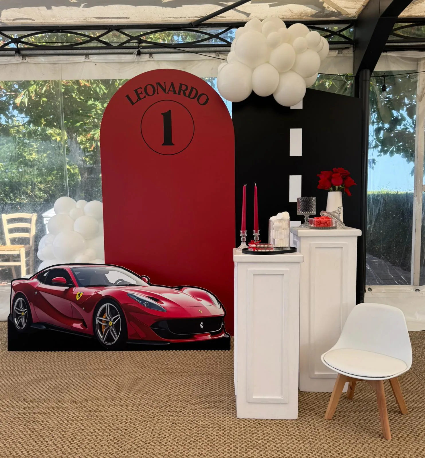 Postazione a tema auto sportive: fondale rosso col nome Leonardo e il numero 1, sagoma della Ferrari a grandezza naturale, pista nera e colonnine bianche
