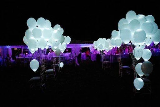 Mazzi di palloncini bianchi luminosi a led legati alle sedie del ricevimento, accesi nel buio della sera