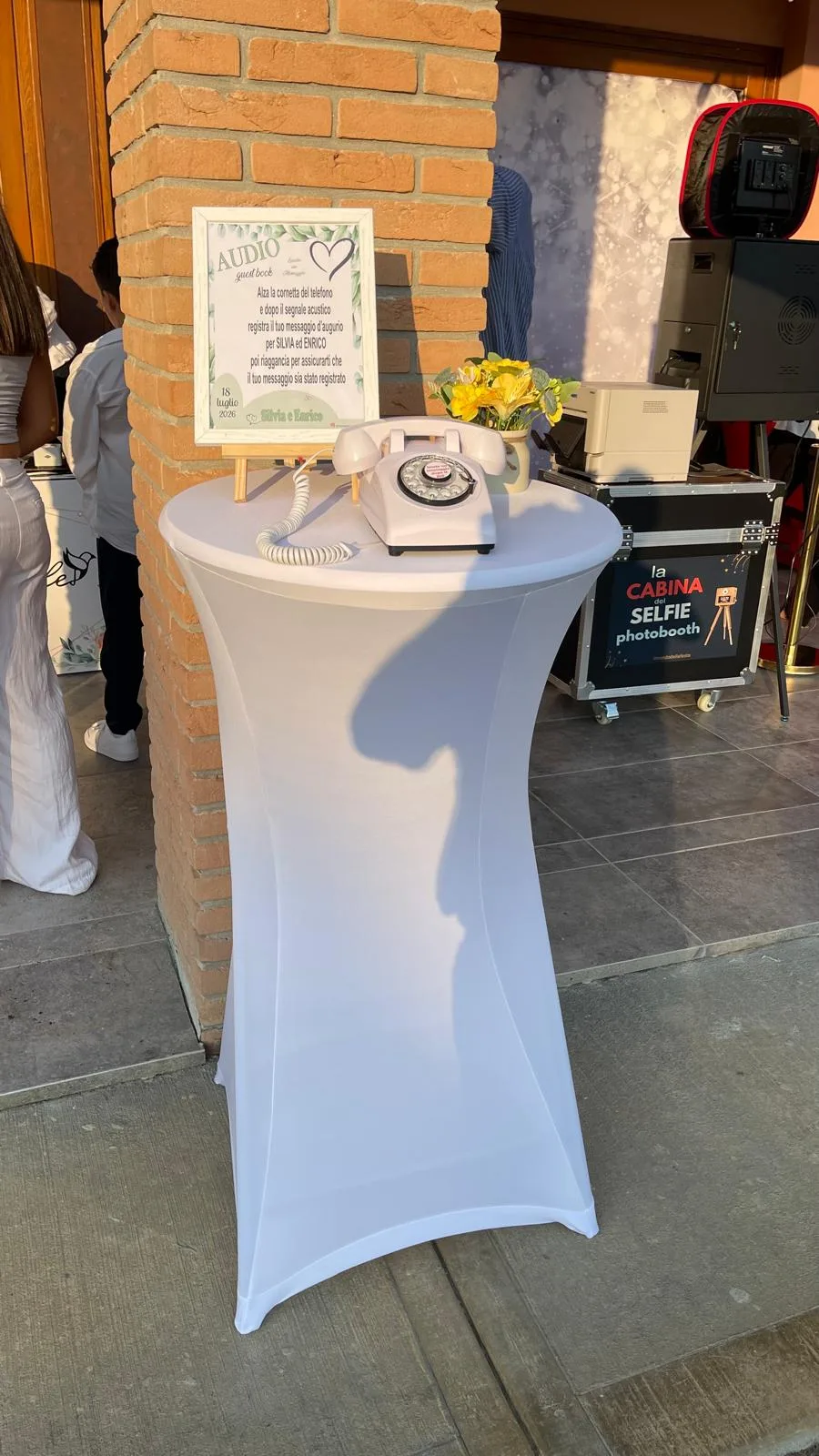 Tavolo alto con telefono vintage e cartello dell'audio guest book vicino all'ingresso, con accanto il baule della Cabina del Selfie