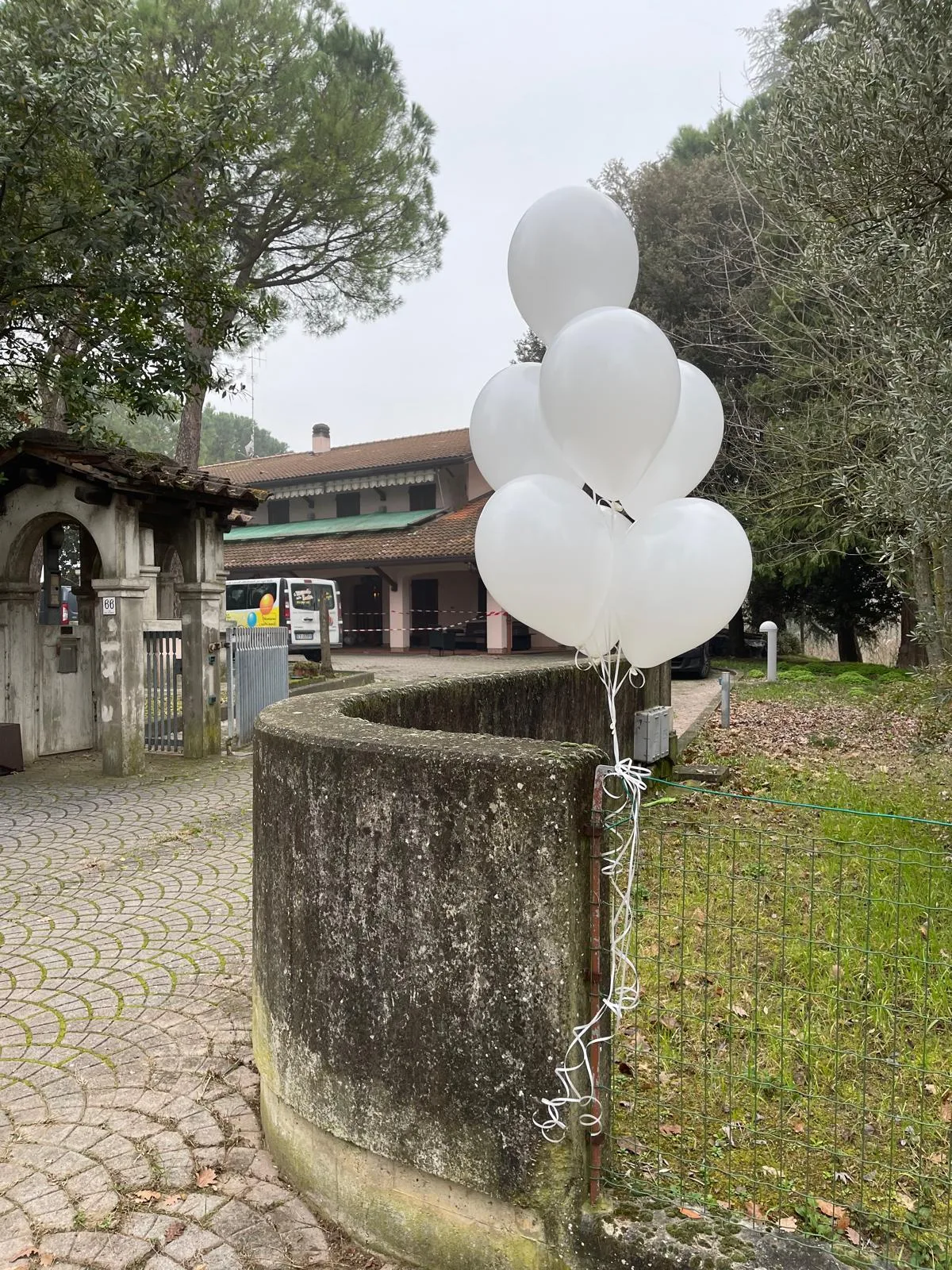 Mazzo di palloncini bianchi a elio legato al cancello di una casa di campagna, per segnalare agli invitati la casa della sposa