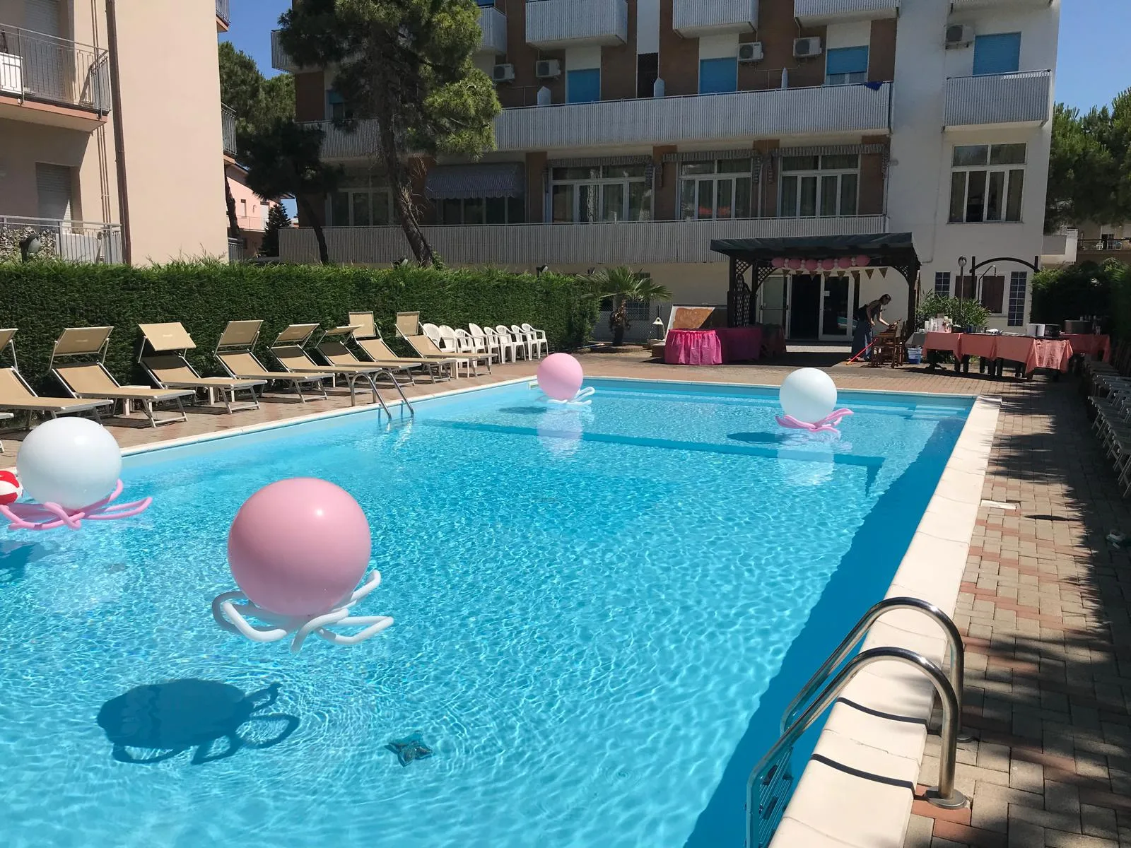 Grandi sfere rosa e bianche appoggiate su fiori di palloncini che galleggiano nella piscina di un hotel, pronte per il ricevimento