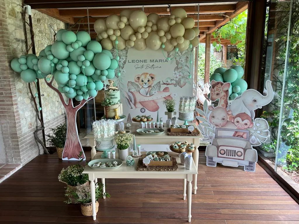 Postazione per un battesimo: pannello col nome Leone Maria, albero di palloncini verde acqua, sagome degli animali e tavolo della confettata