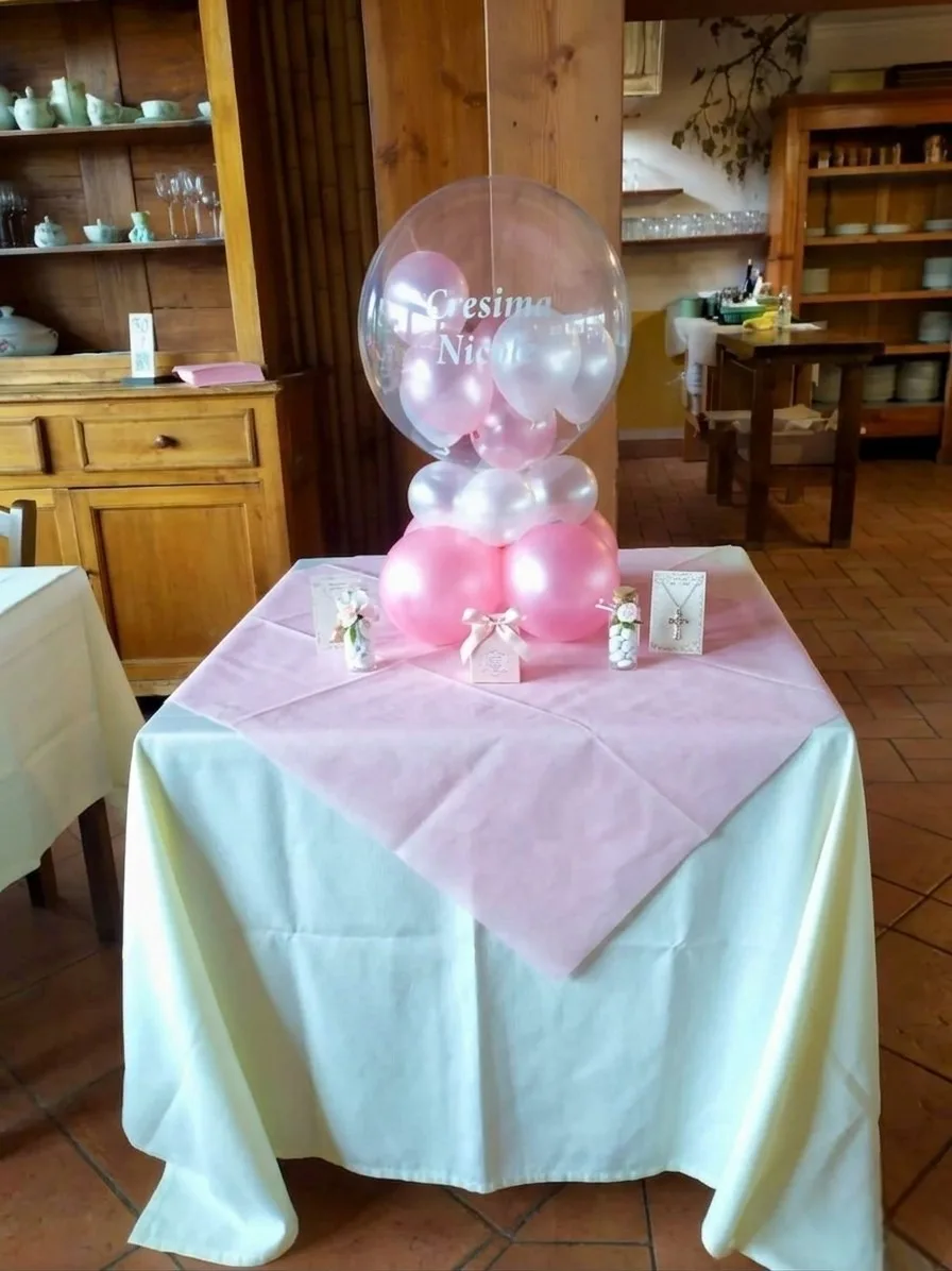 Tavolo dei confetti con palloncino bubble trasparente scritto Cresima Nicole, su una base di palloncini rosa e bianchi perlati