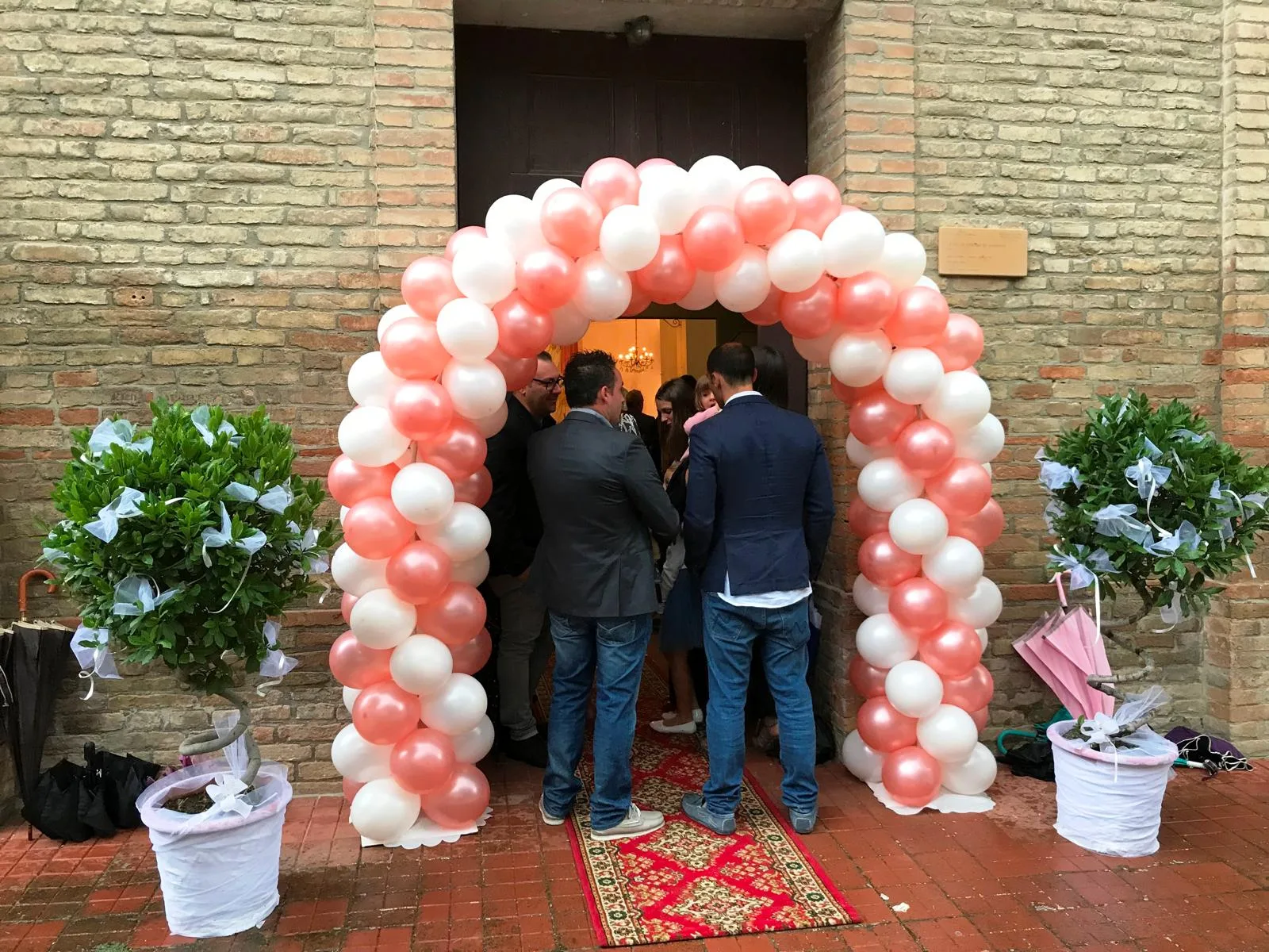 Arco di palloncini rosa e bianchi montato sul portone della chiesa, con alberelli in vaso decorati di tulle ai lati