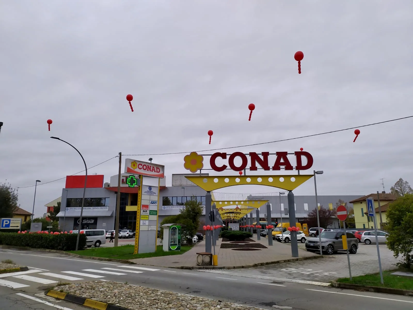 Palloncini rossi a elio con grappoli sollevati sopra il piazzale di un supermercato e ghirlanda di palloncini rossi lungo la siepe del parcheggio