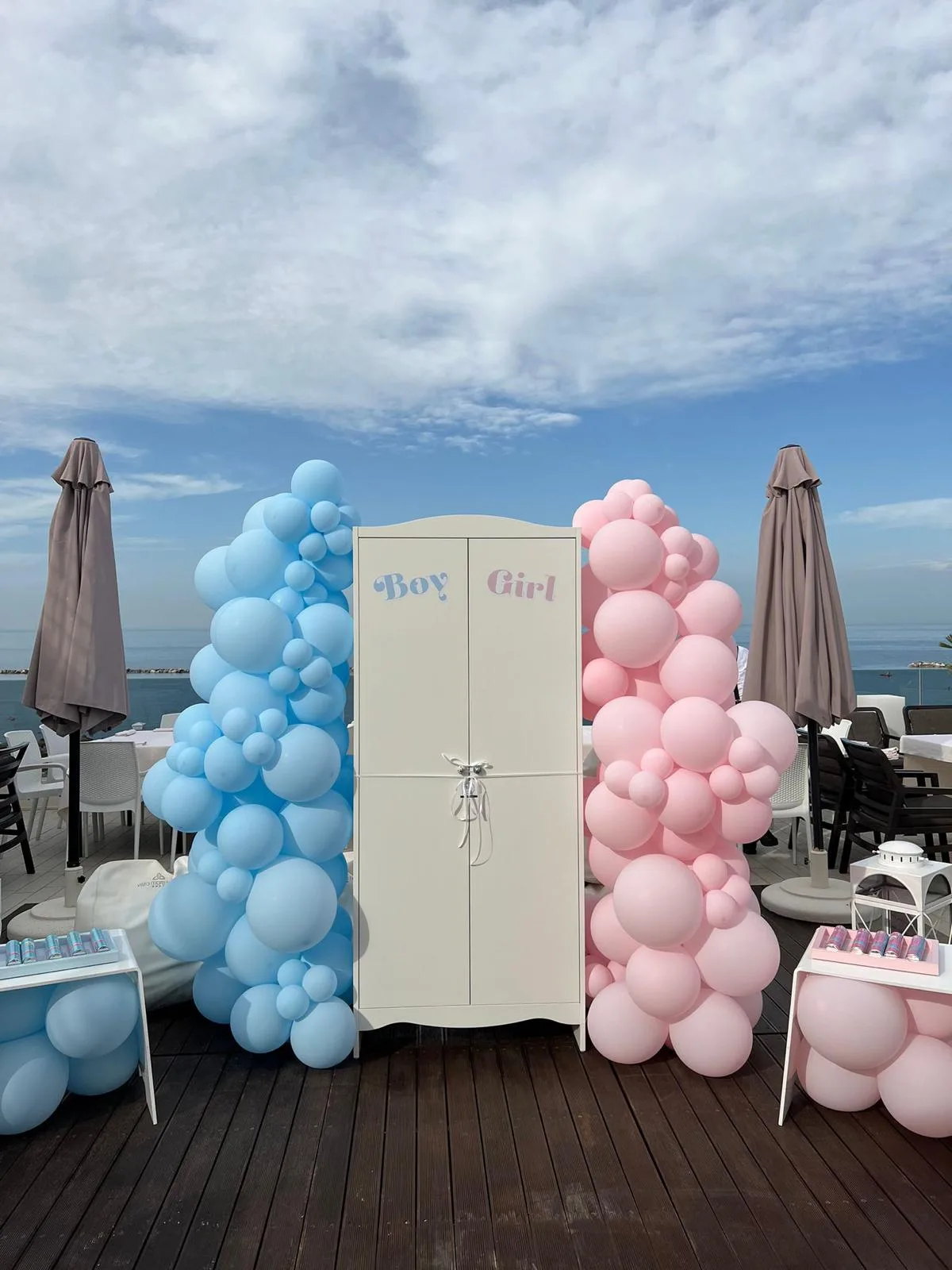 Gender reveal in stabilimento sul mare con armadio bianco Boy e Girl e due colonne di palloncini, una azzurra e una rosa, sulla terrazza in legno