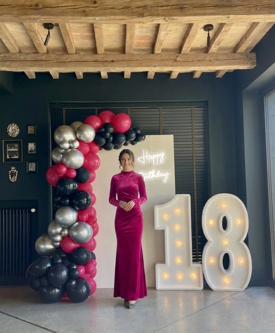 Postazione per un diciottesimo: numeri 1 e 8 luminosi, pannello con scritta Happy Birthday al neon e arco di palloncini fucsia, neri e argento