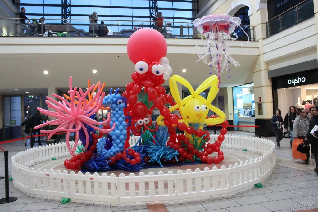 Scenografia marina di palloncini in galleria: polpo rosso con sfera gigante, pesci azzurri e gialli, anemone rosa, coralli e medusa sospesa