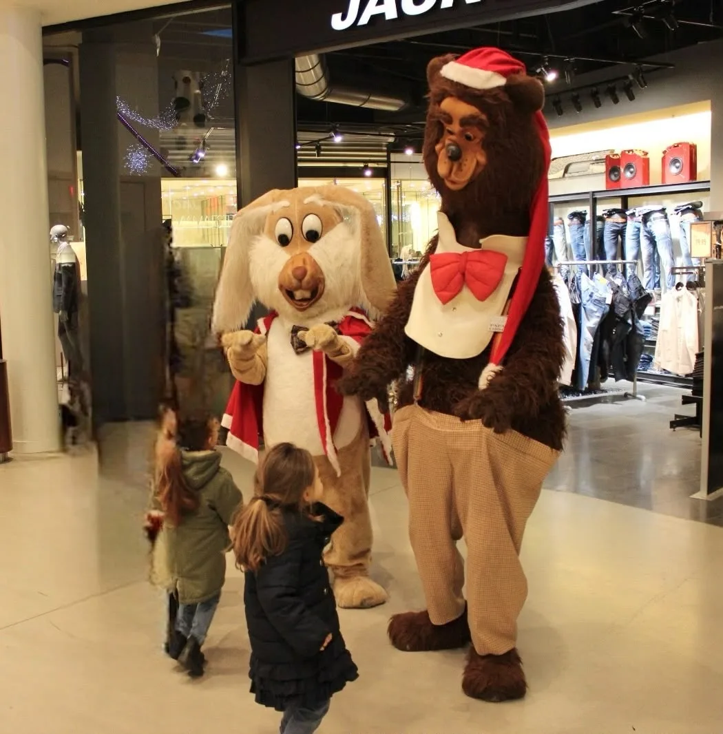 Le mascotte del coniglio e dell'orso con cappello di Natale salutano due bambine in una galleria commerciale