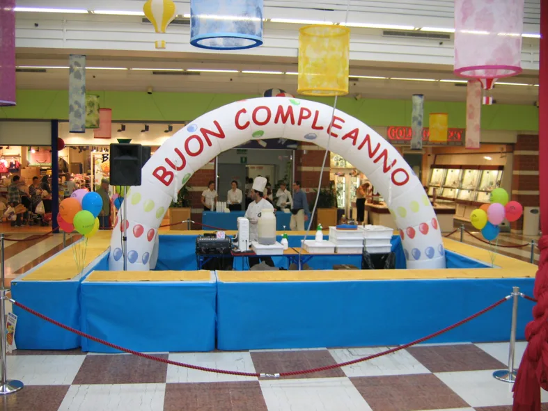 Arco gonfiabile bianco con la scritta «Buon compleanno» sopra un'area recintata in azzurro con il pasticcere al lavoro
