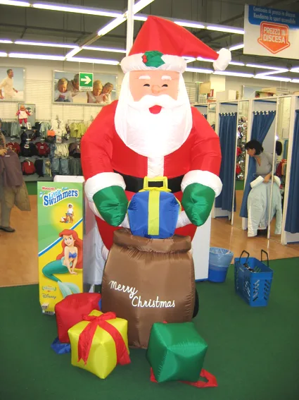 Babbo Natale gonfiabile con il sacco dei regali e i pacchi colorati, dentro un negozio