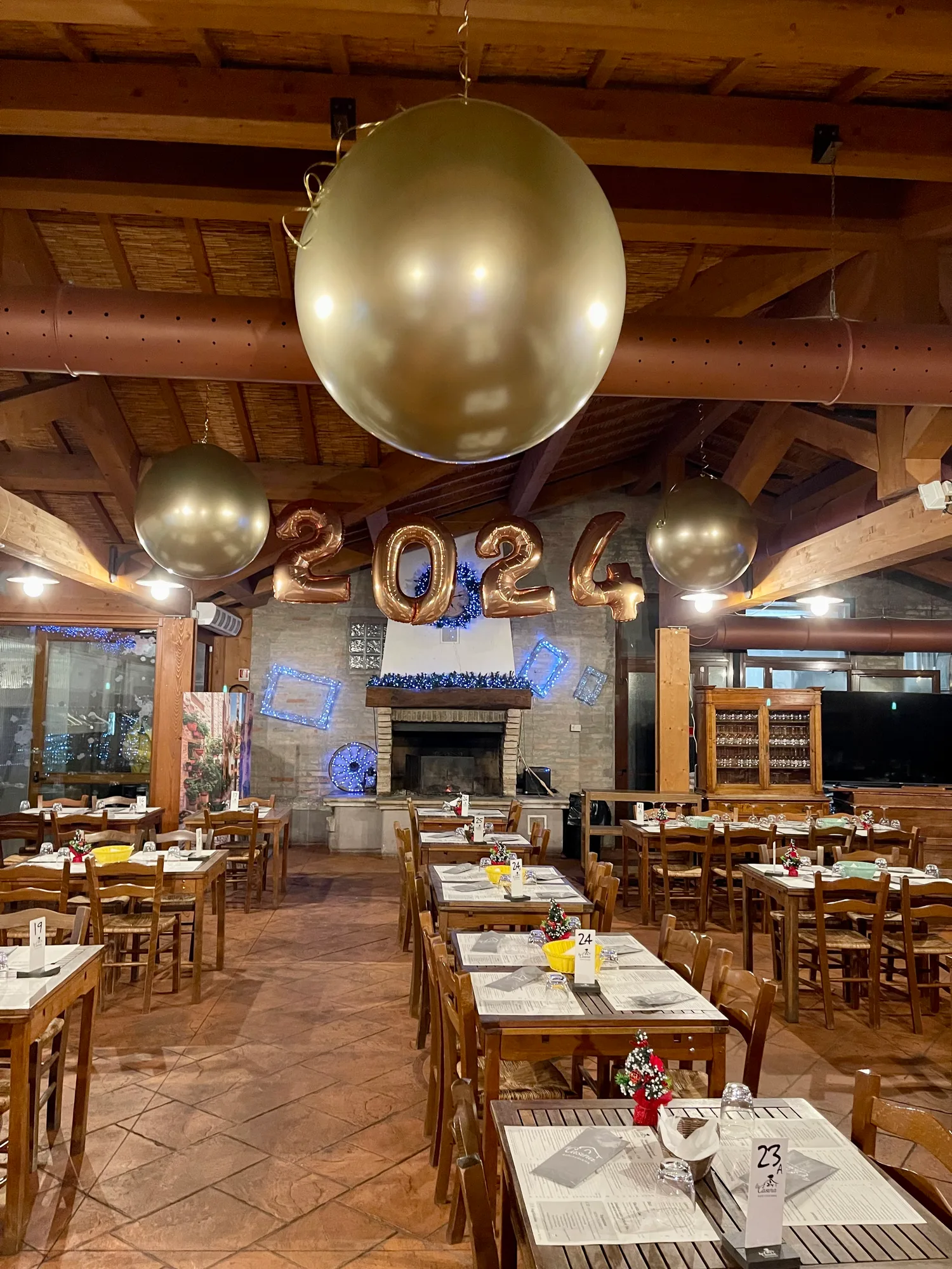 Sfera gigante dorata appesa in primo piano, con i numeri 2024 color oro rosa e altre due sfere sopra i tavoli apparecchiati del ristorante