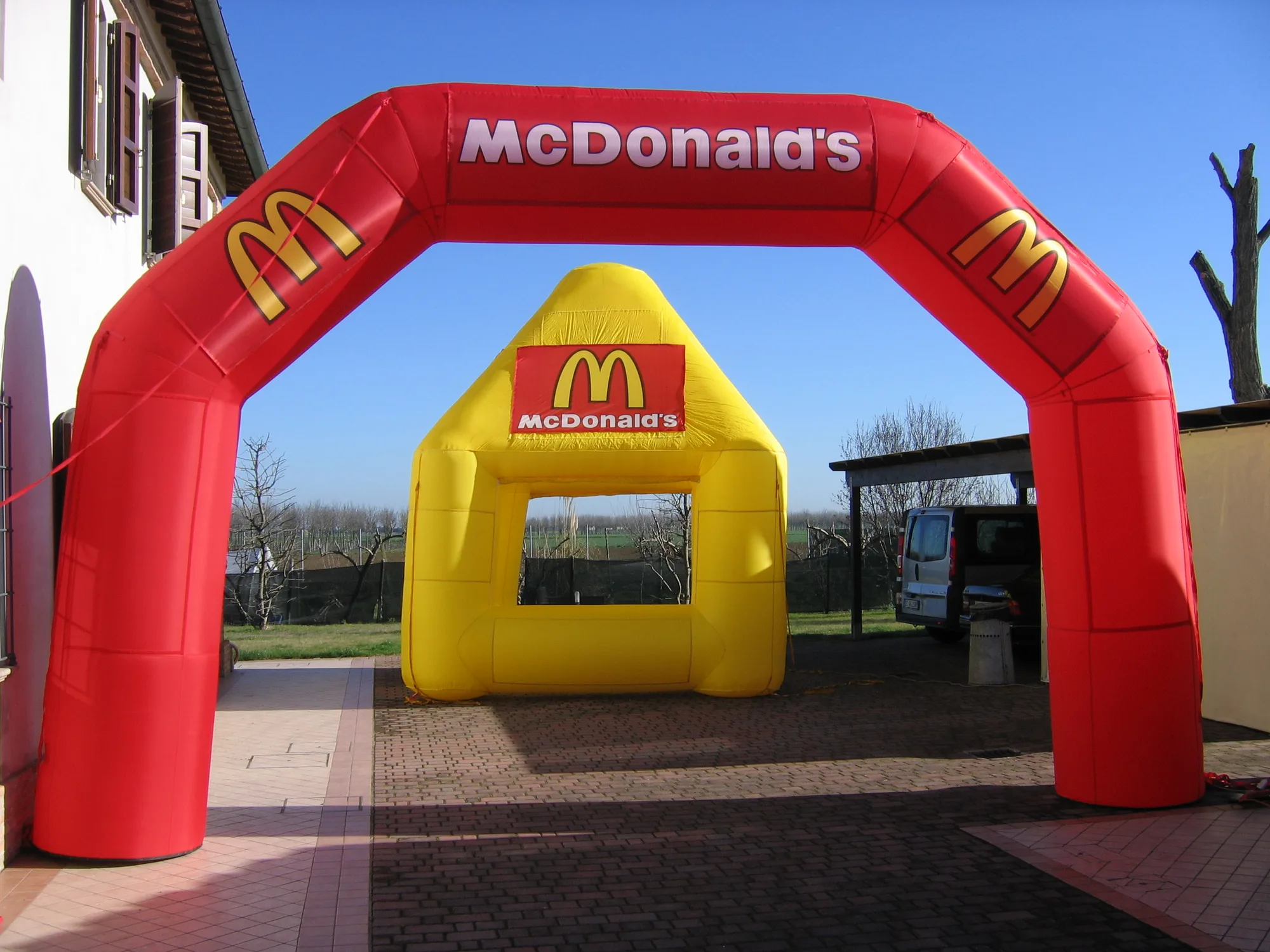Arco gonfiabile rosso personalizzato con il logo di un cliente e, sotto, uno stand gonfiabile giallo con la stessa grafica