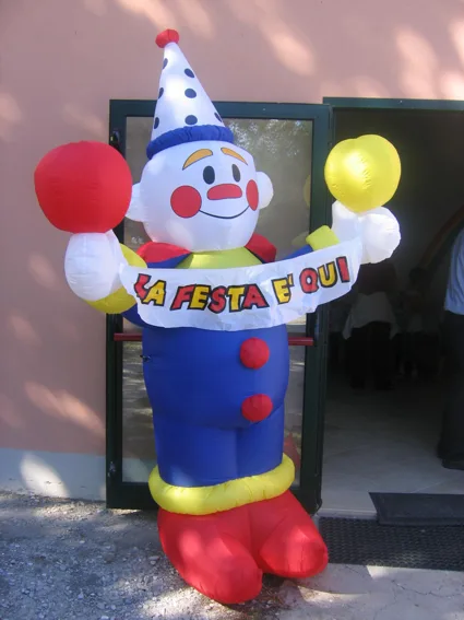 Clown gonfiabile con due palloncini e lo striscione «La festa è qui» davanti a un ingresso