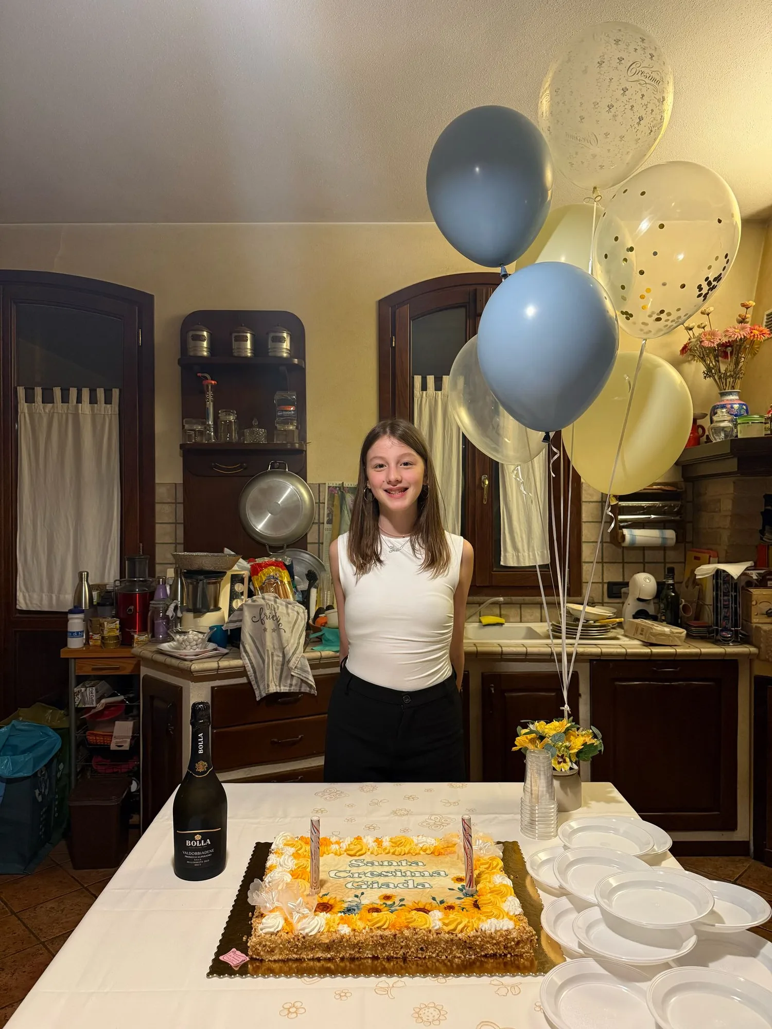 Ragazza dietro alla torta della Santa Cresima con un mazzo di palloncini a elio azzurri, avorio e con coriandoli oro