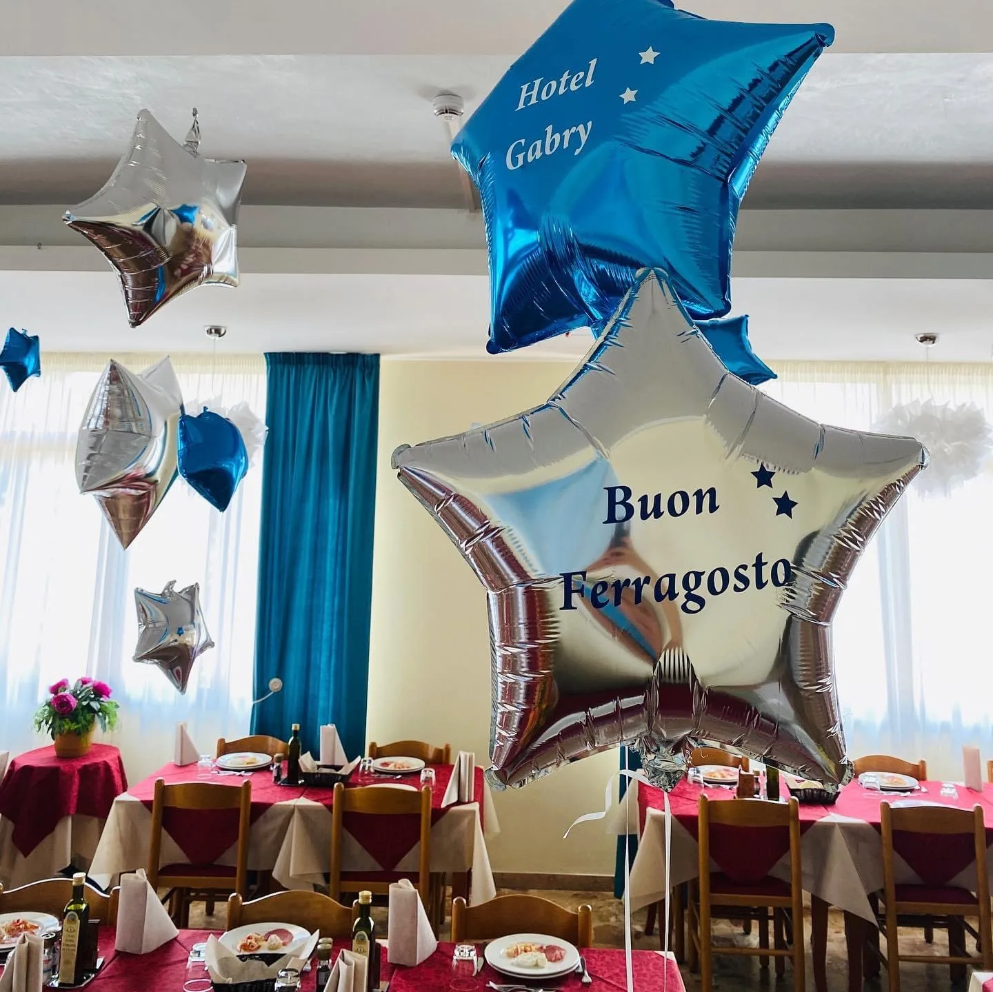 Grande cornice di palloncini verdi con fiori, farfalle, una coccinella e un'ape, e la scritta Hotel La Falena, con una ragazza in posa al centro