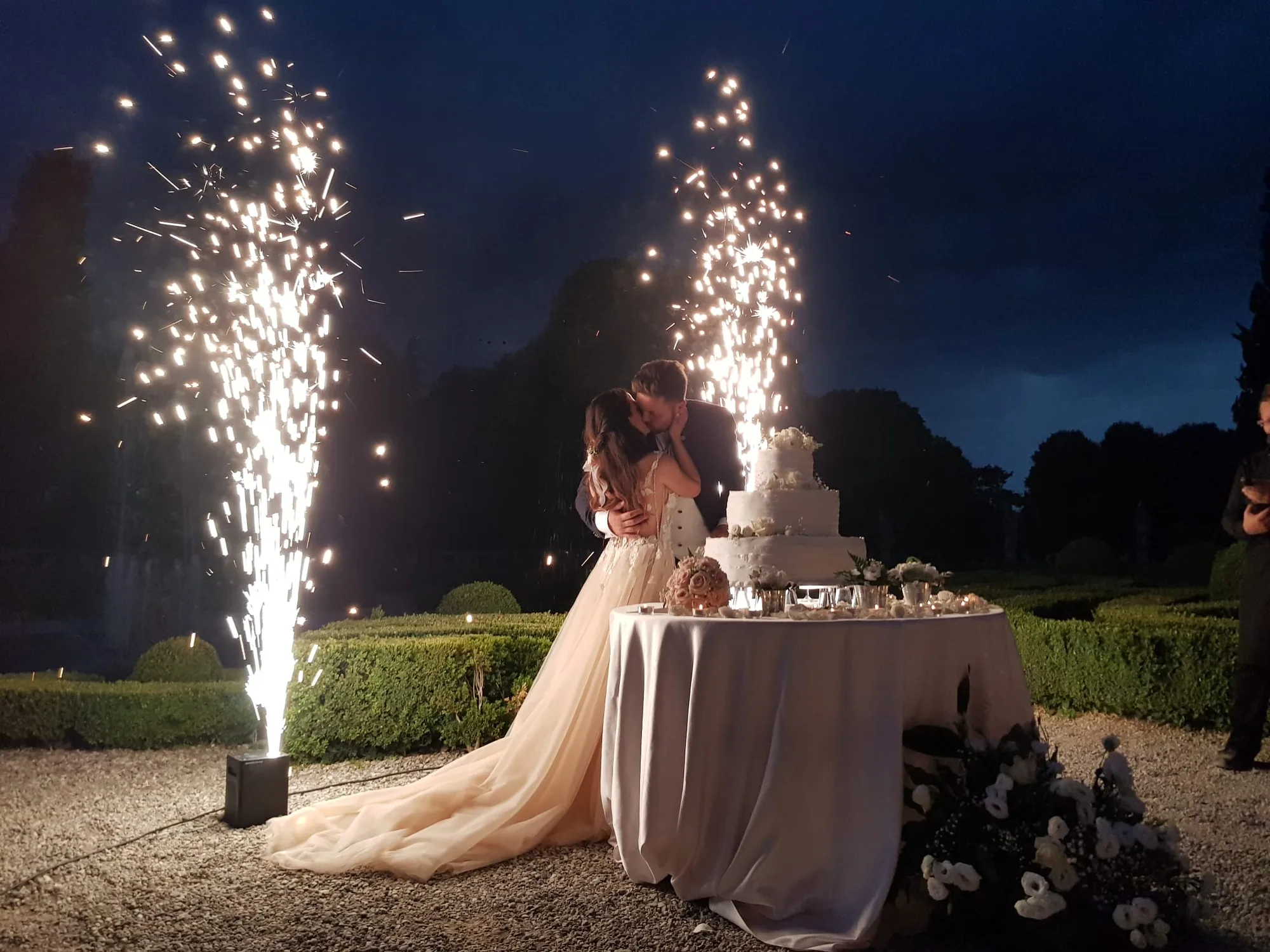 Due fontane scintillanti accese di sera ai lati della torta nuziale, mentre gli sposi si baciano in un giardino all'italiana