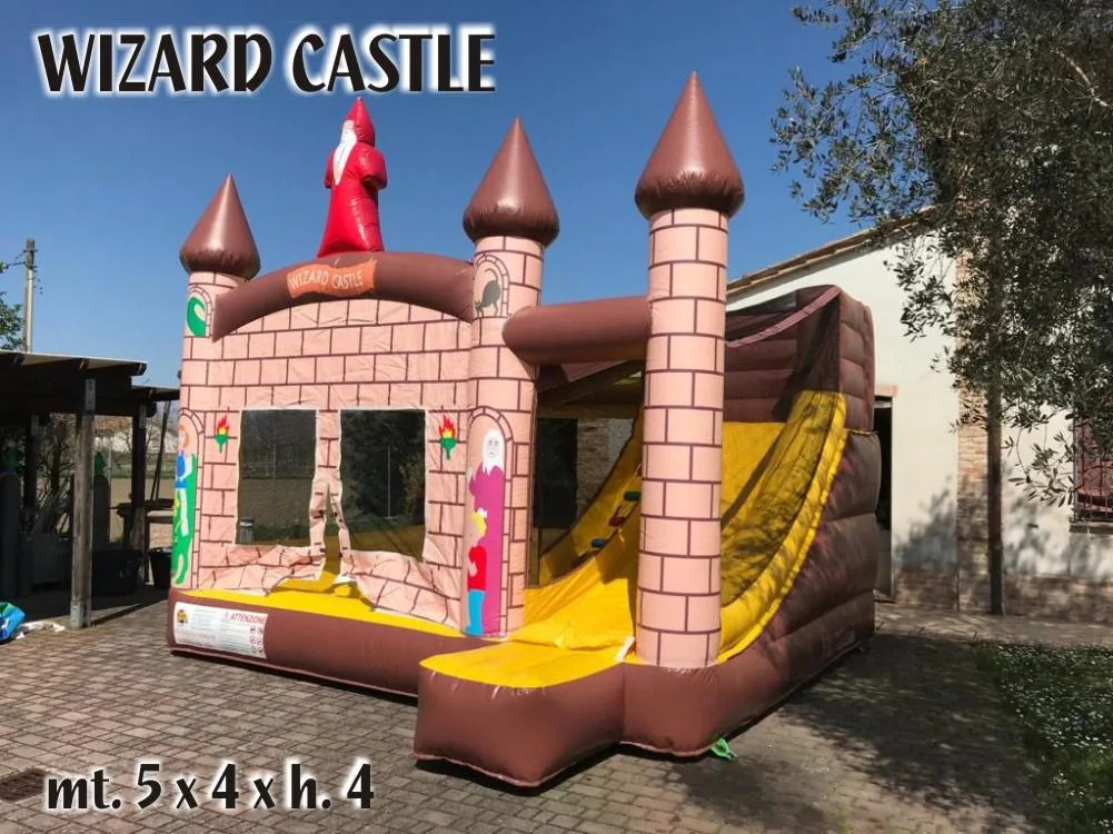 Castello di Camelot gonfiabile visto di tre quarti in un cortile: torri a mattoni rosa con i tetti a punta marroni, il mago rosso sul tetto e lo scivolo giallo sul fianco