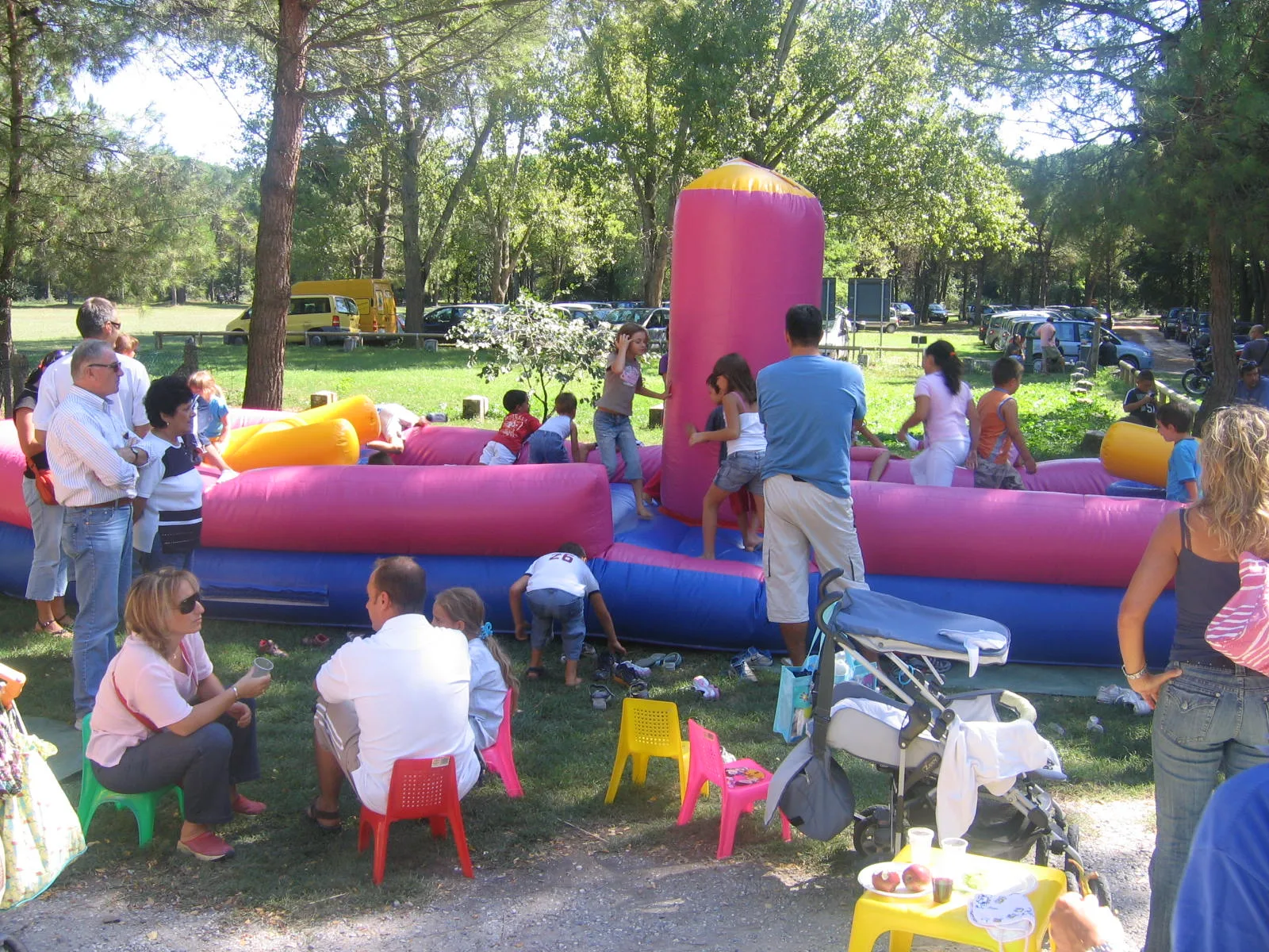 Bambini che giocano sul Tira e Molla durante una festa in una pineta, con genitori seduti sulle seggioline colorate tutto intorno