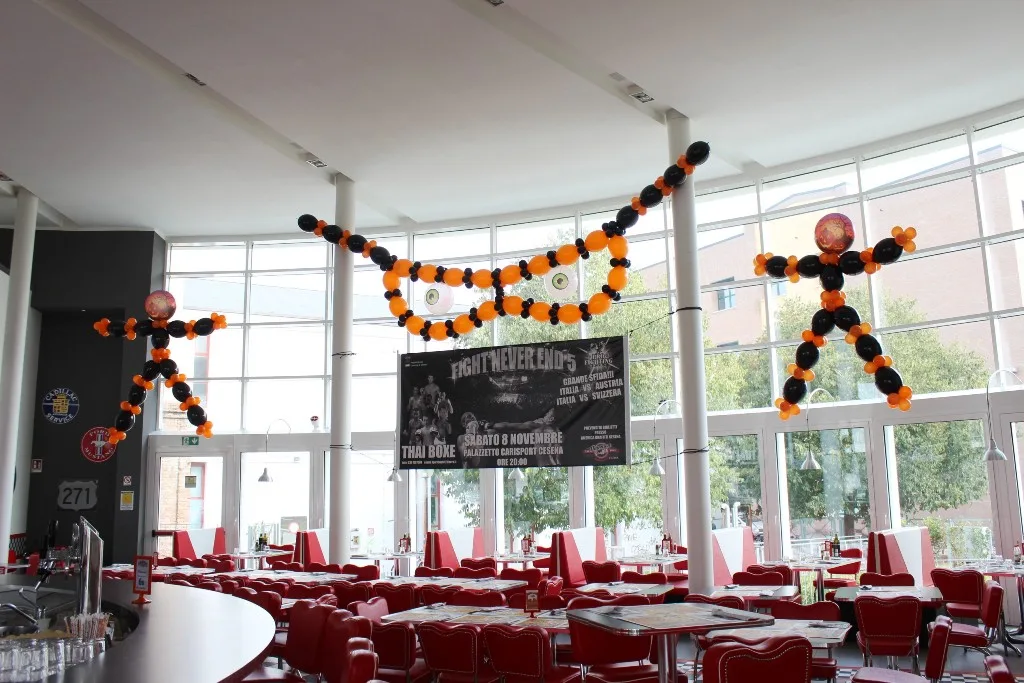 Scheletri e una figura con gli occhi fatti di palloncini arancio e neri appesi sopra i tavoli di un locale