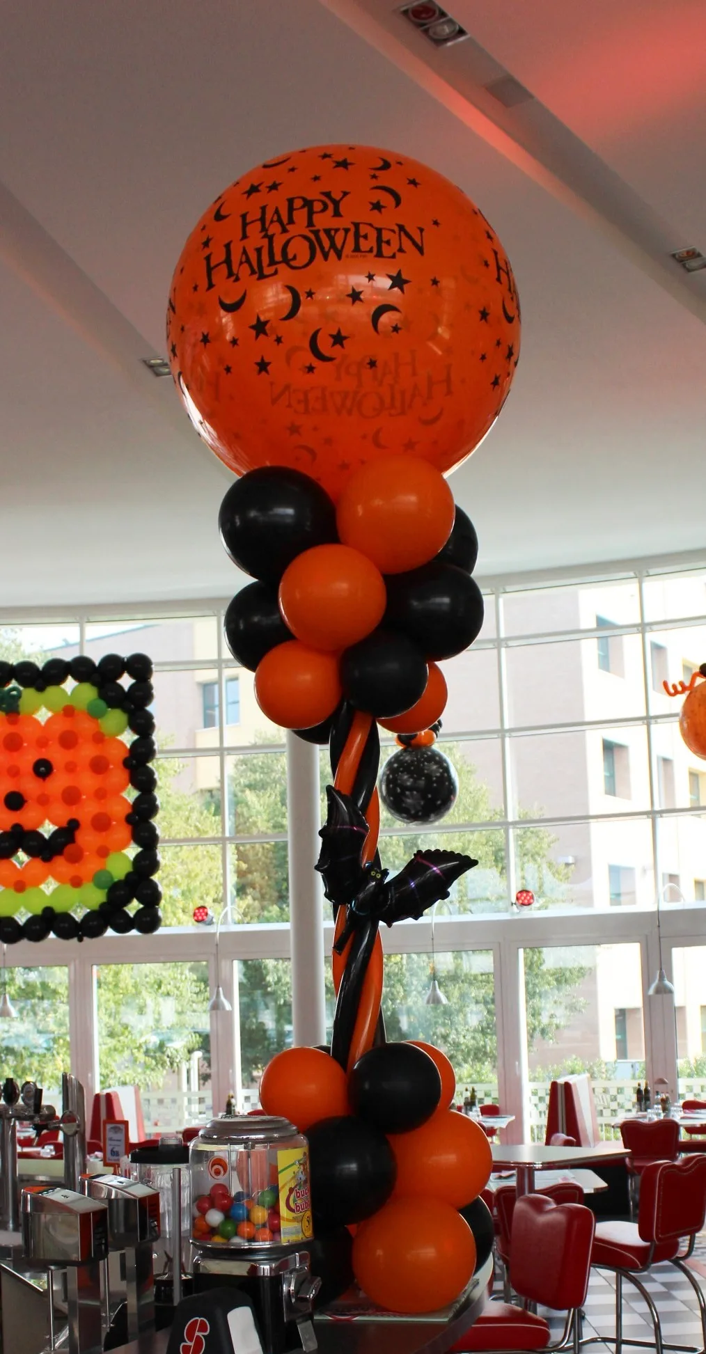 Colonna di palloncini arancio e neri con un pipistrello in mylar e in cima un grande palloncino arancione con la scritta Happy Halloween