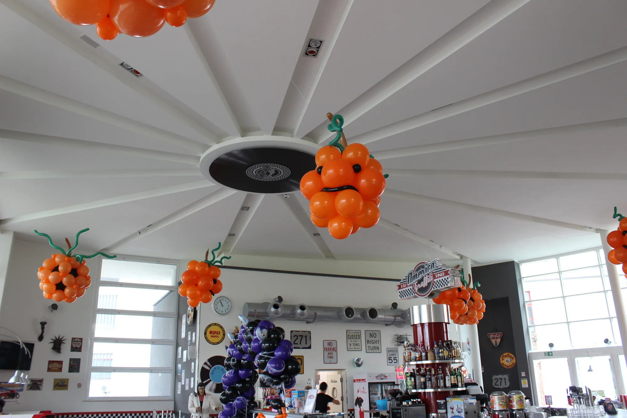 Zucche di palloncini arancioni con i gambi verdi appese al soffitto di un locale, sopra una colonna di palloncini viola e neri