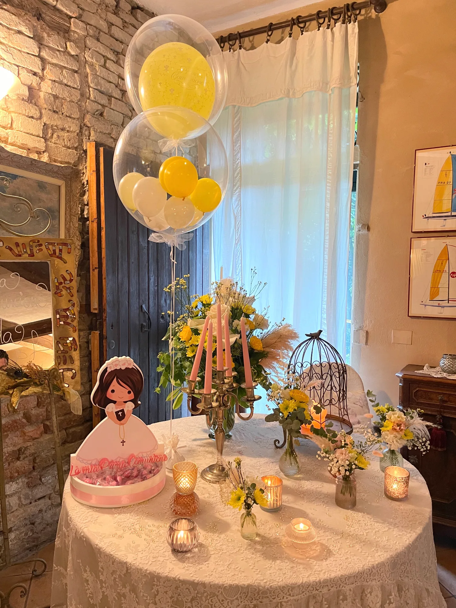 Allestimento di palloncini preparato per una festa di comunione, con composizione nei toni chiari accanto al tavolo del ricevimento