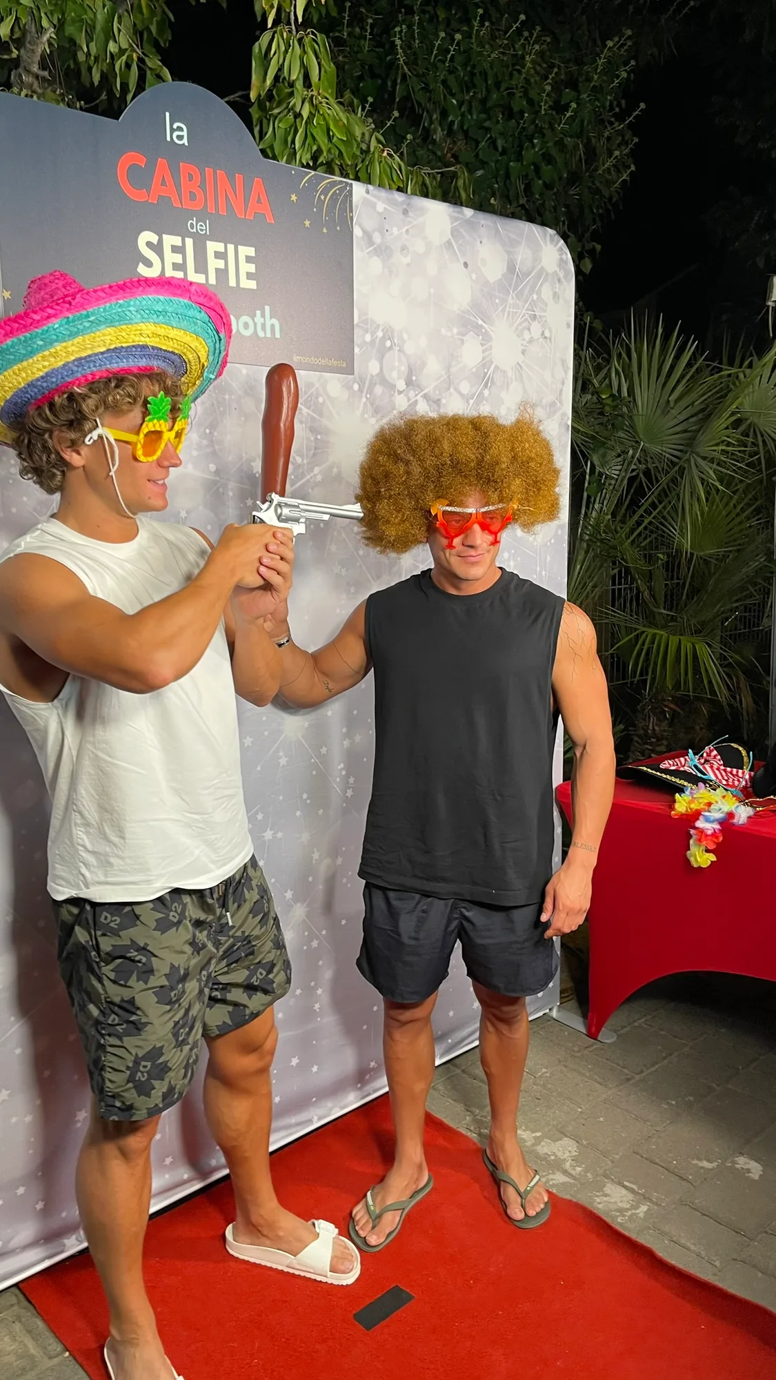 Due ragazzi scherzano davanti alla cabina con sombrero, parrucca afro e occhiali colorati presi dal cesto degli accessori