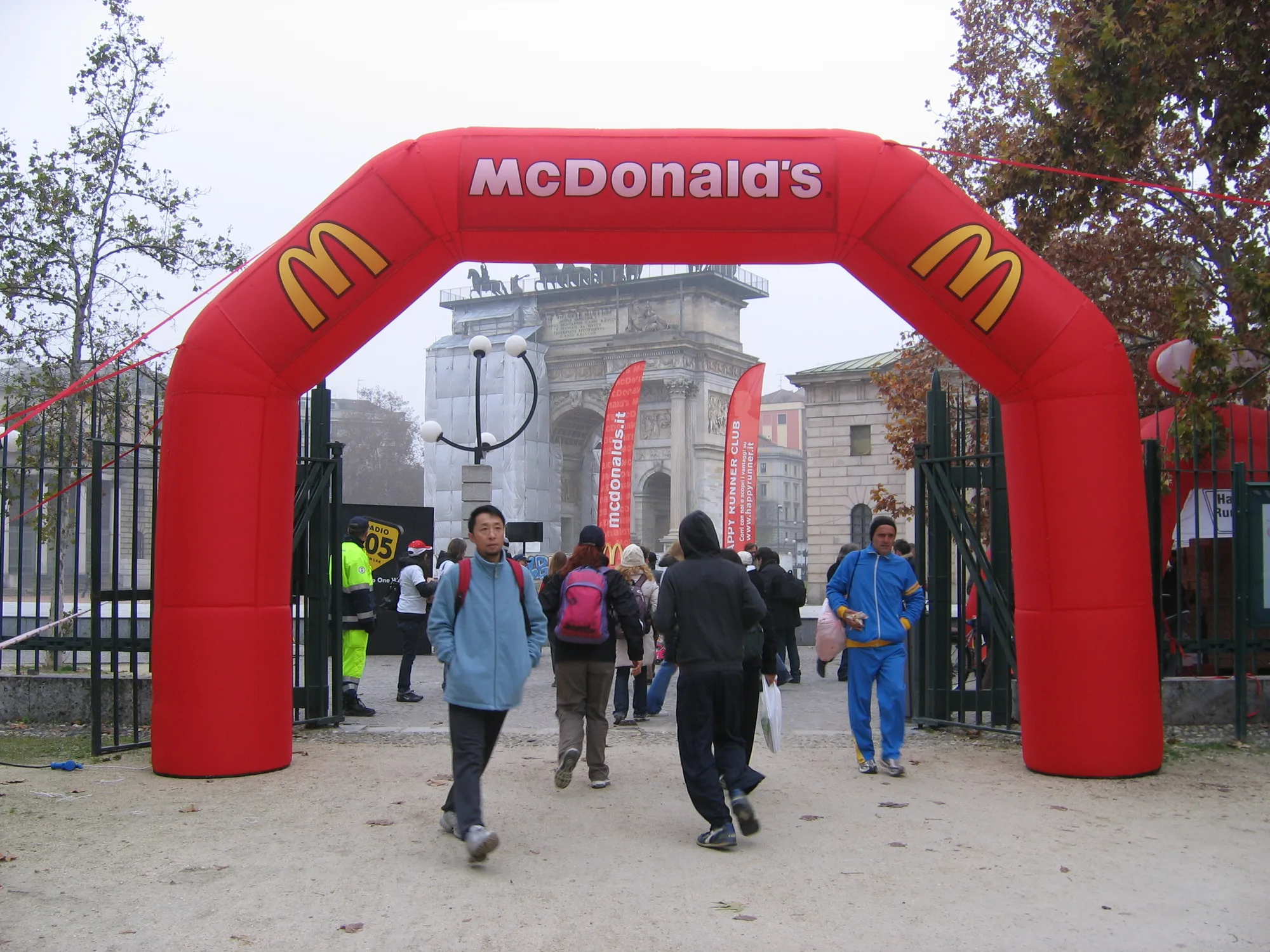 Grande arco gonfiabile rosso personalizzato all'ingresso di un parco in città, con i partecipanti di una camminata che lo attraversano