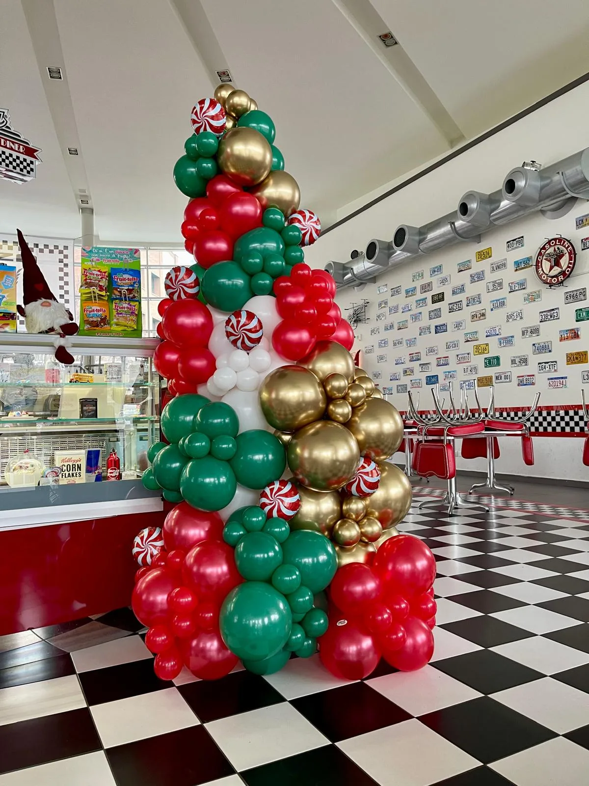 Albero di Natale alto circa due metri fatto di palloncini rossi, verdi, bianchi e oro con caramelle decorative, in un ristorante