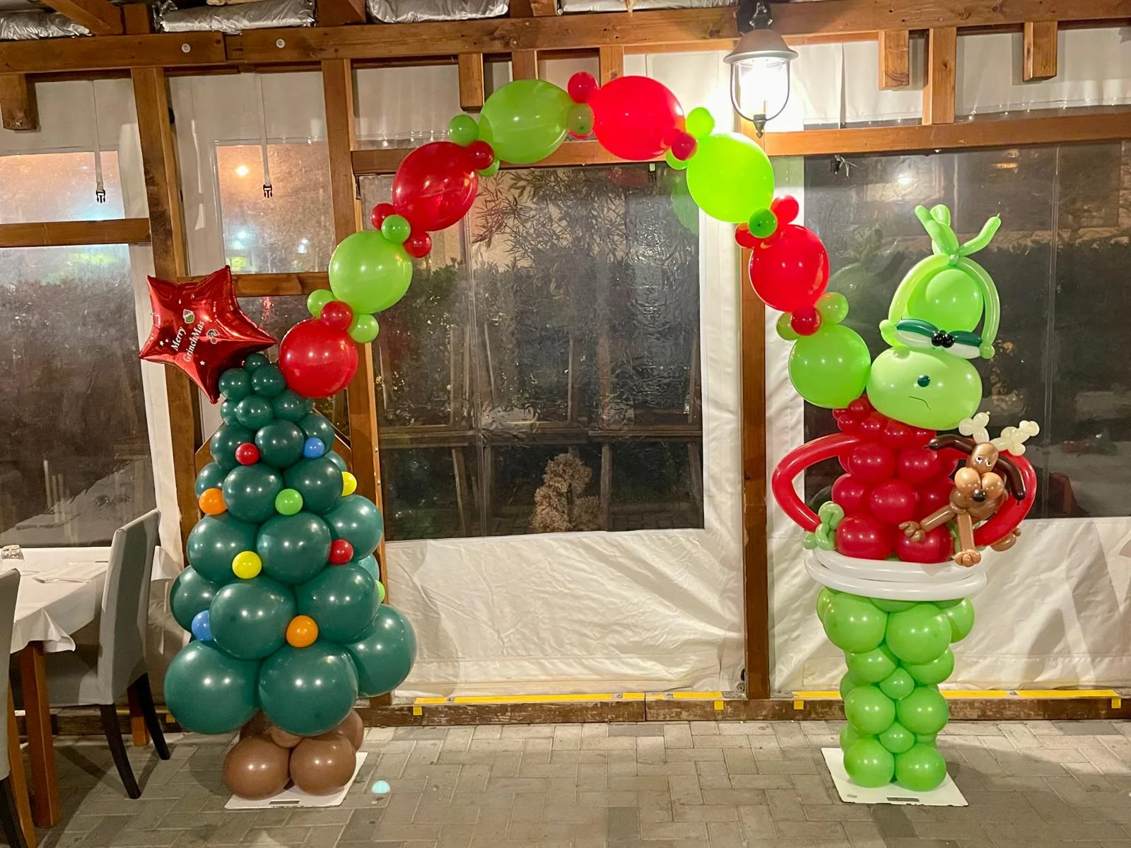 Arco di palloncini verdi e rossi tra un albero di Natale di palloncini con la stella Merry GrinchMas e un personaggio verde di palloncini con il cappello da Babbo Natale