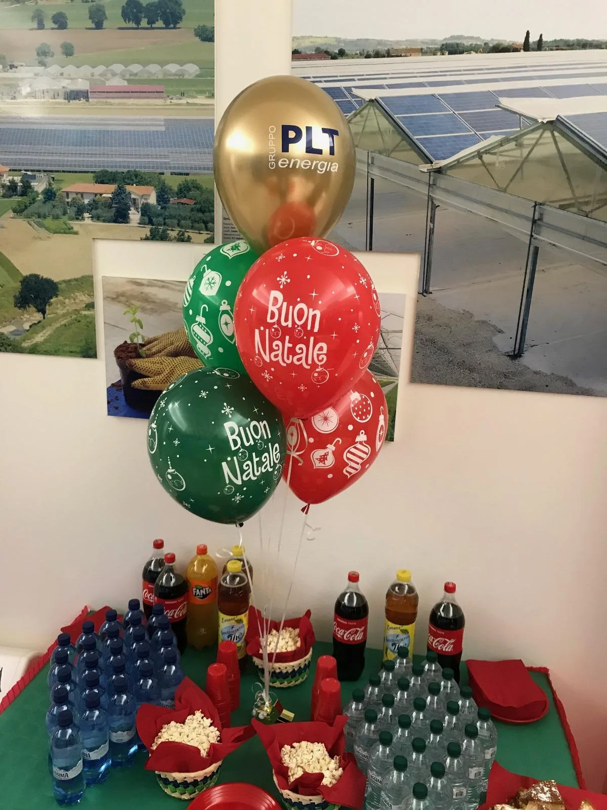 Bouquet di palloncini rossi e verdi con la scritta Buon Natale e un palloncino oro con il logo di un'azienda, sopra un buffet