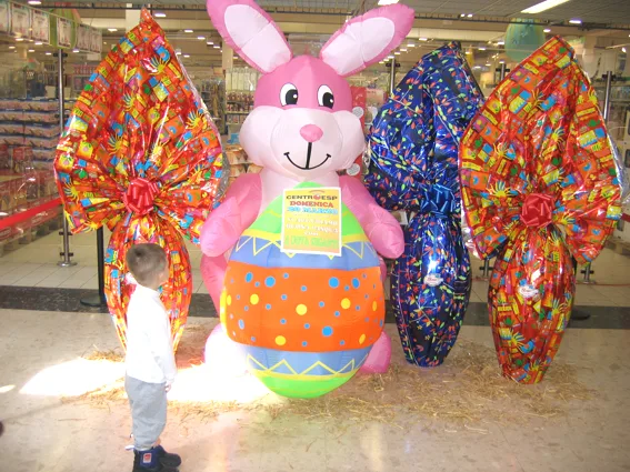 Coniglio gonfiabile rosa con un grande uovo colorato, circondato da uova di Pasqua giganti in un centro commerciale