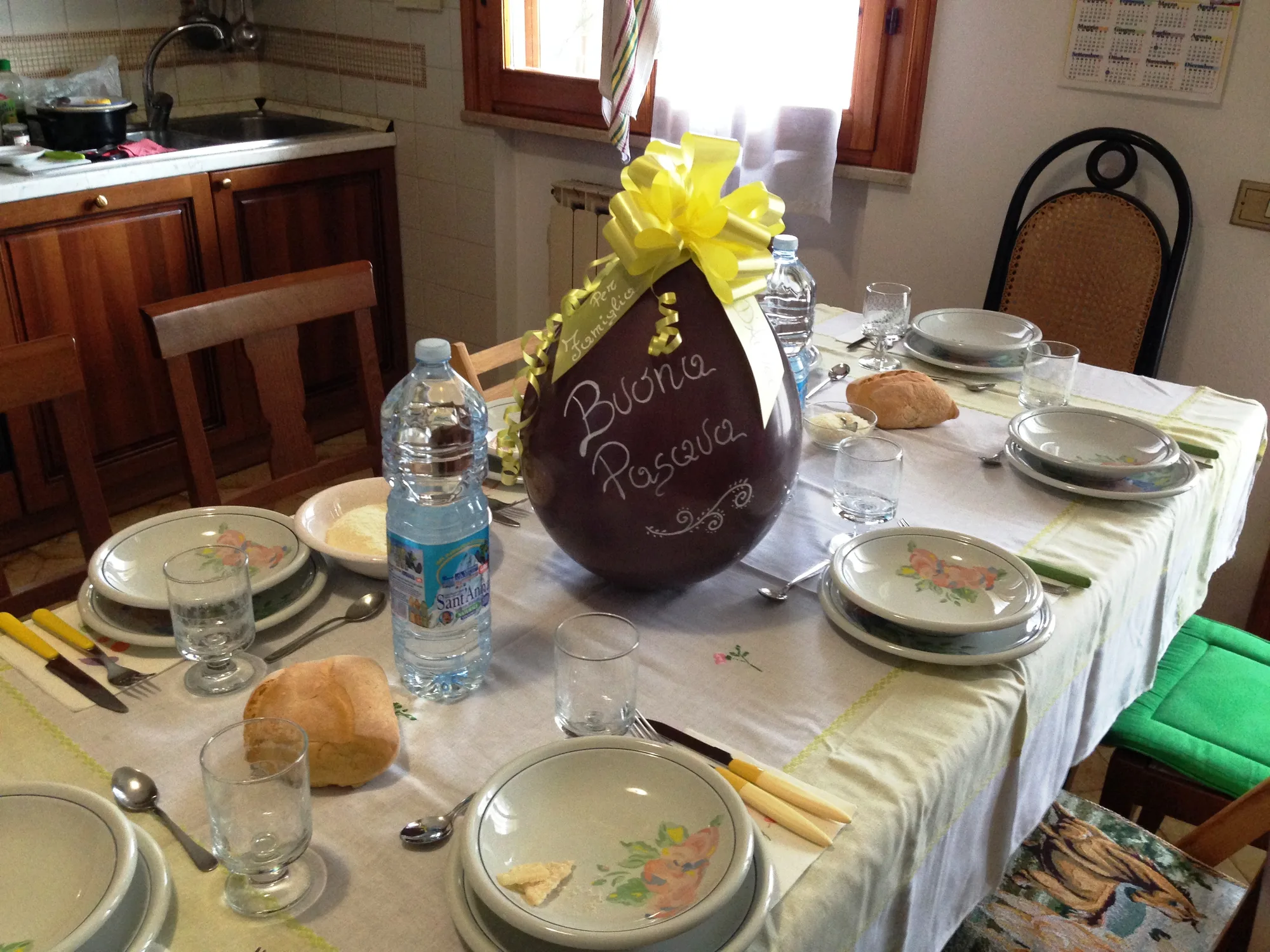 Grande palloncino marrone a forma di uovo con la scritta Buona Pasqua e un fiocco giallo, al centro di una tavola apparecchiata