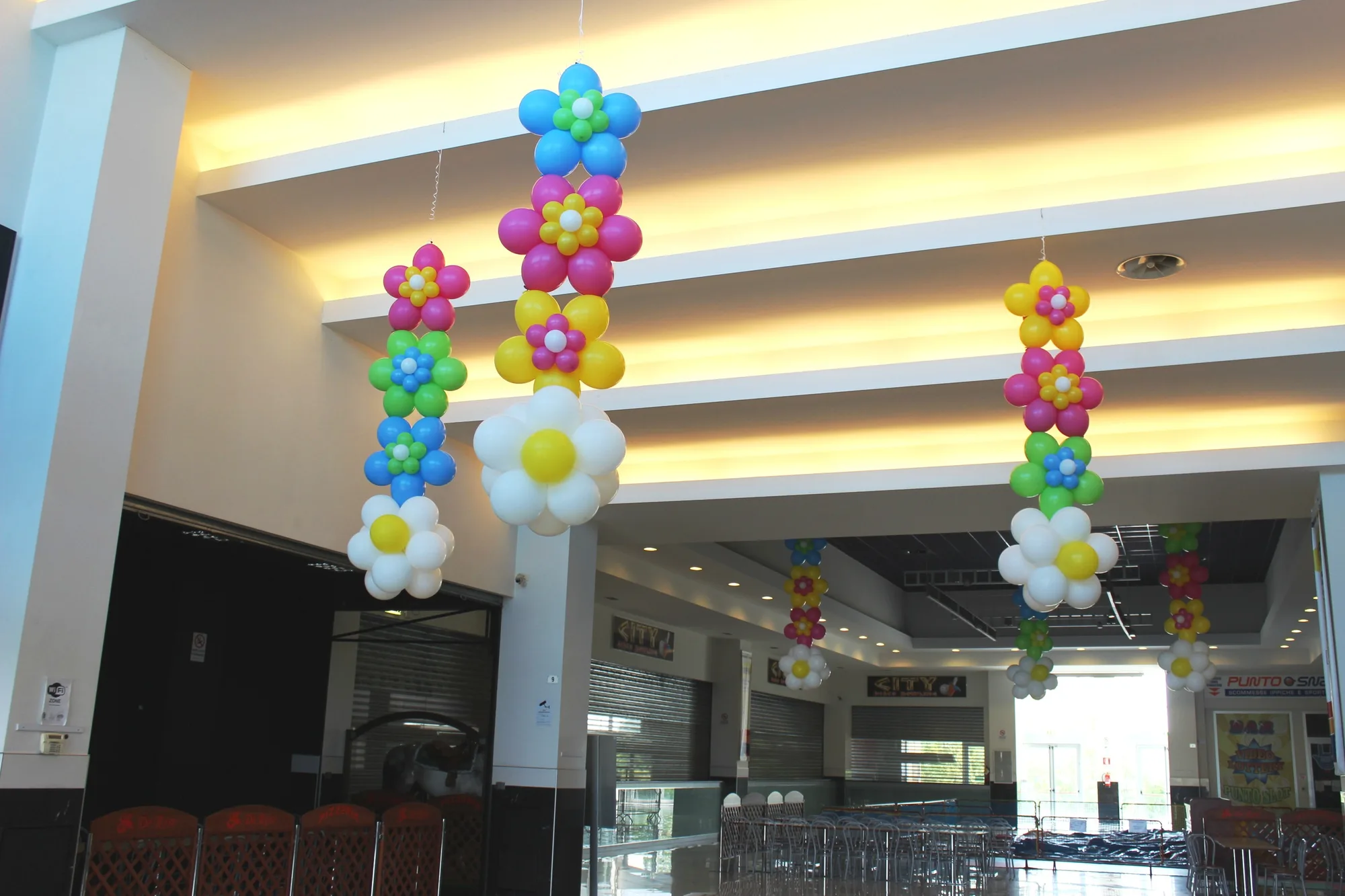 Catene di fiori di palloncini colorati e margherite bianche appese al soffitto di una galleria commerciale