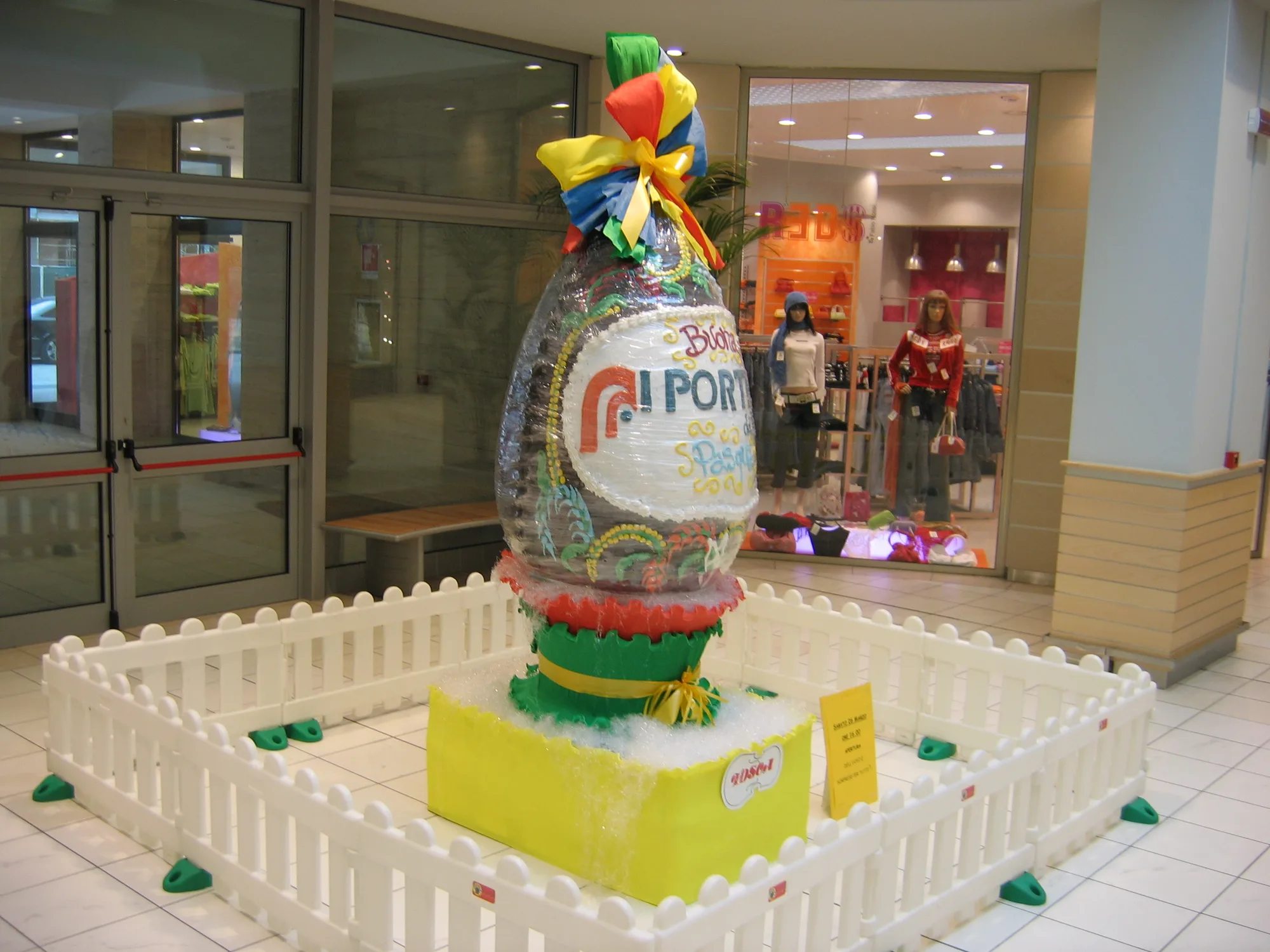 Uovo di Pasqua gigante incartato dentro una recinzione di transennine bianche in una galleria commerciale