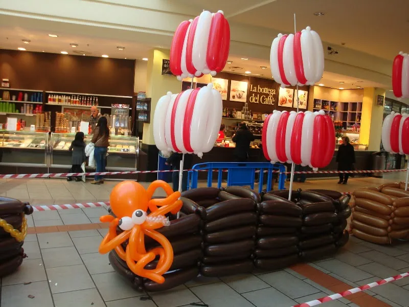 Nave pirata costruita con palloncini marroni, con le vele a strisce rosse e bianche e un polpo arancione, in una galleria commerciale