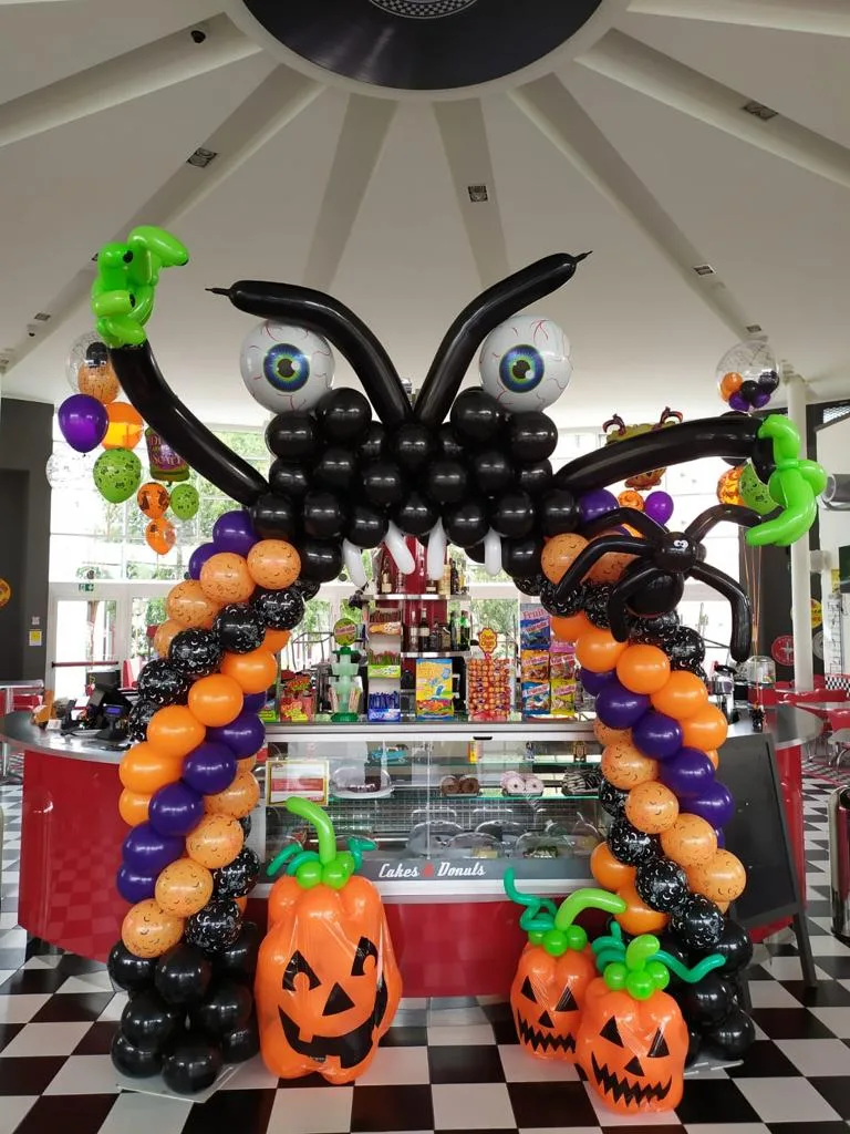 Arco completo di palloncini neri, viola e arancioni con zucche e ragno gigante, montato all'ingresso di un locale per Halloween