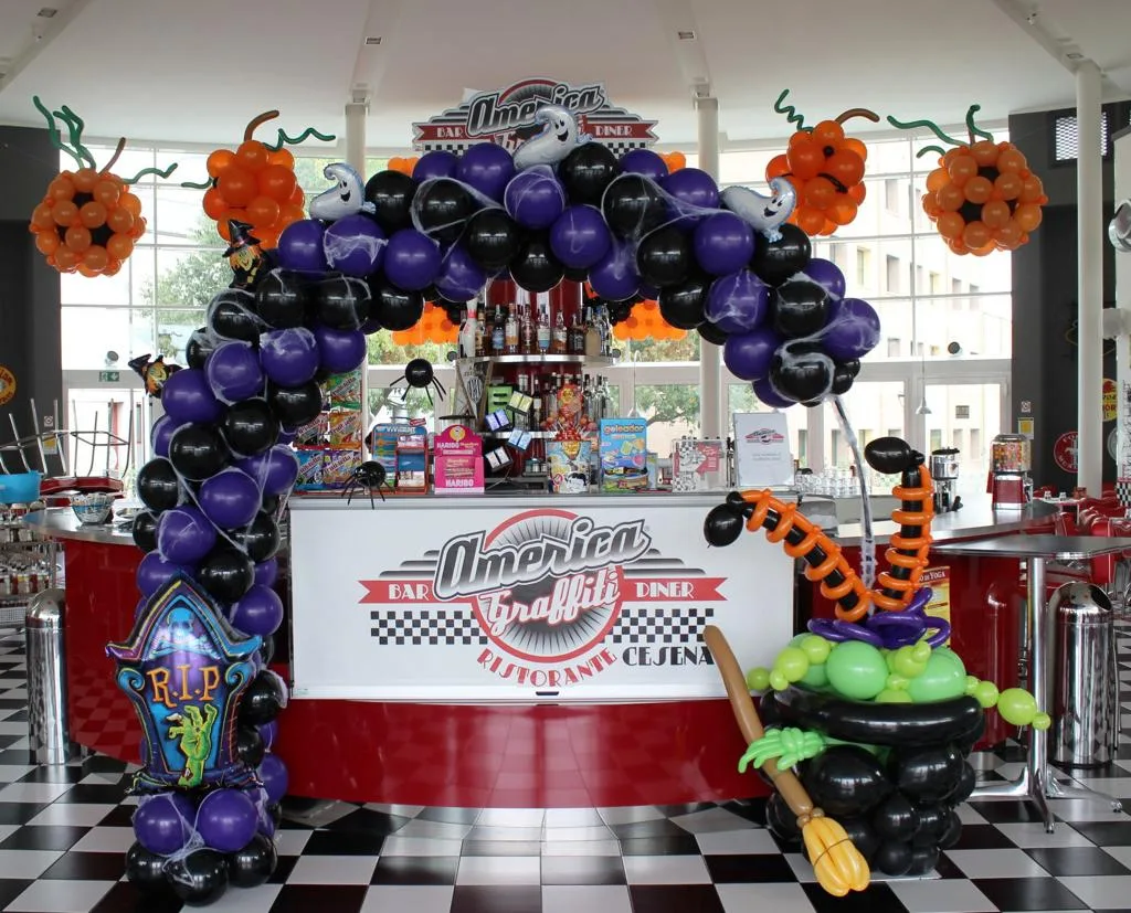 Arco di palloncini viola e neri con fantasmi, zucche e un calderone di palloncini all'ingresso di un ristorante