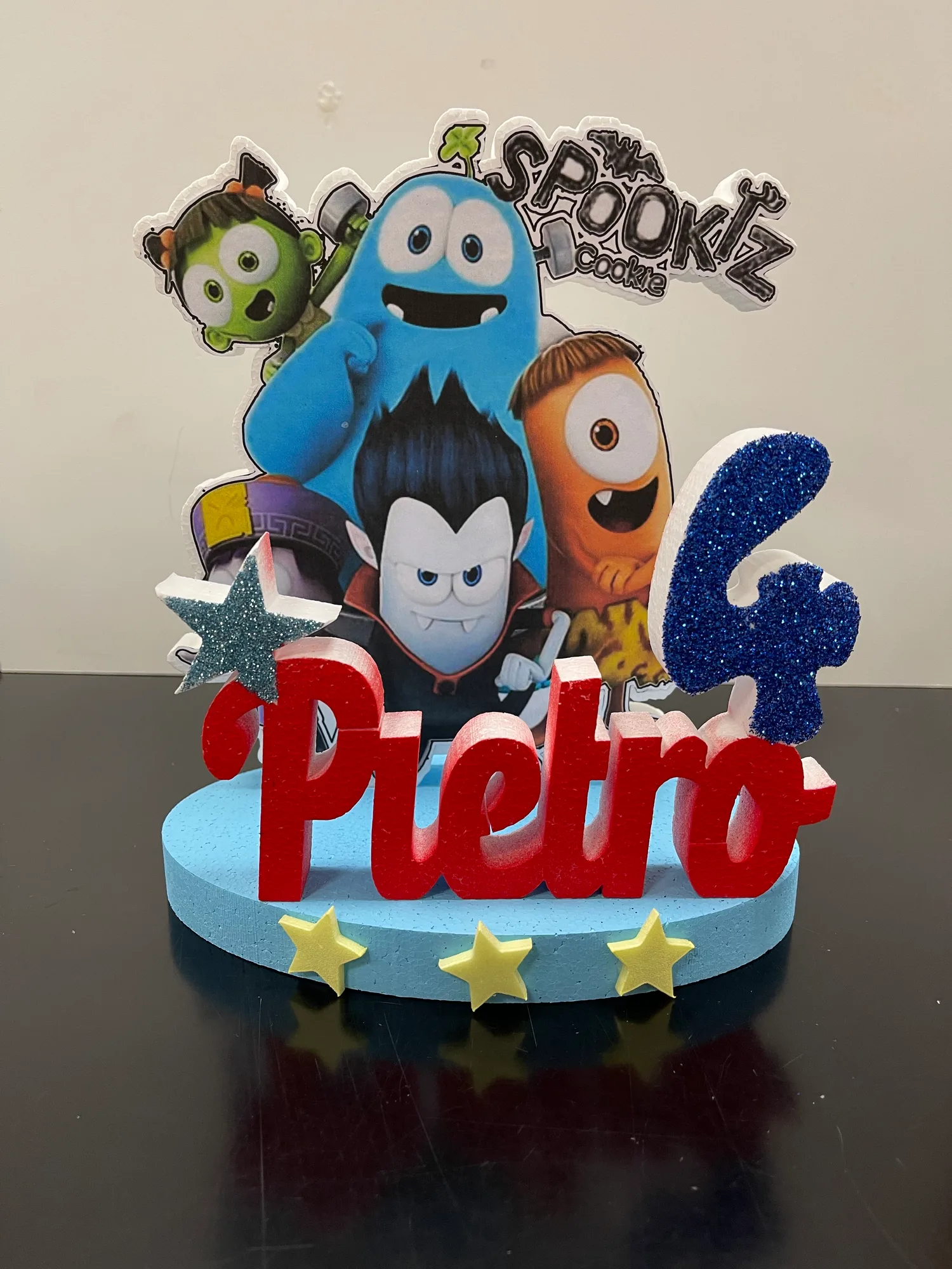 Sagoma in polistirolo con personaggi dei cartoni stampati, il nome Pietro in lettere rosse, il numero 4 blu glitterato e stelle gialle su una base azzurra
