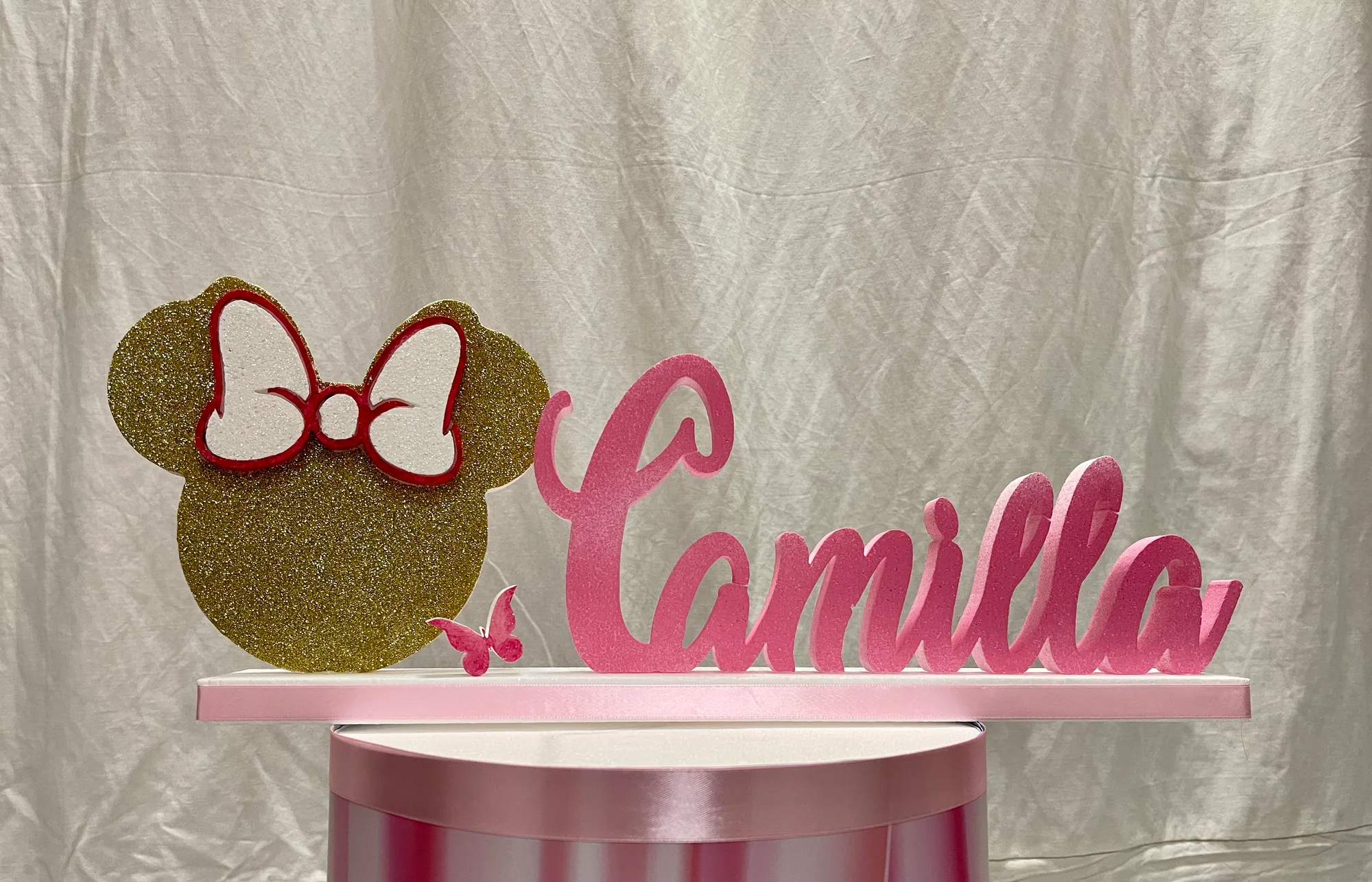 Testa di topolina in polistirolo oro glitterato con fiocco bianco e rosso, una farfalla e il nome Camilla in lettere rosa su una base bianca e rosa