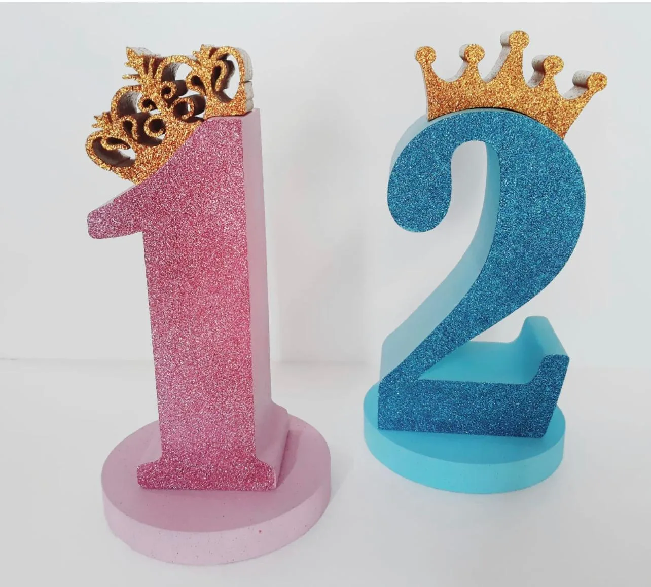 Numero 1 rosa e numero 2 azzurro in polistirolo glitterato, ognuno con una corona oro, su basi tonde abbinate